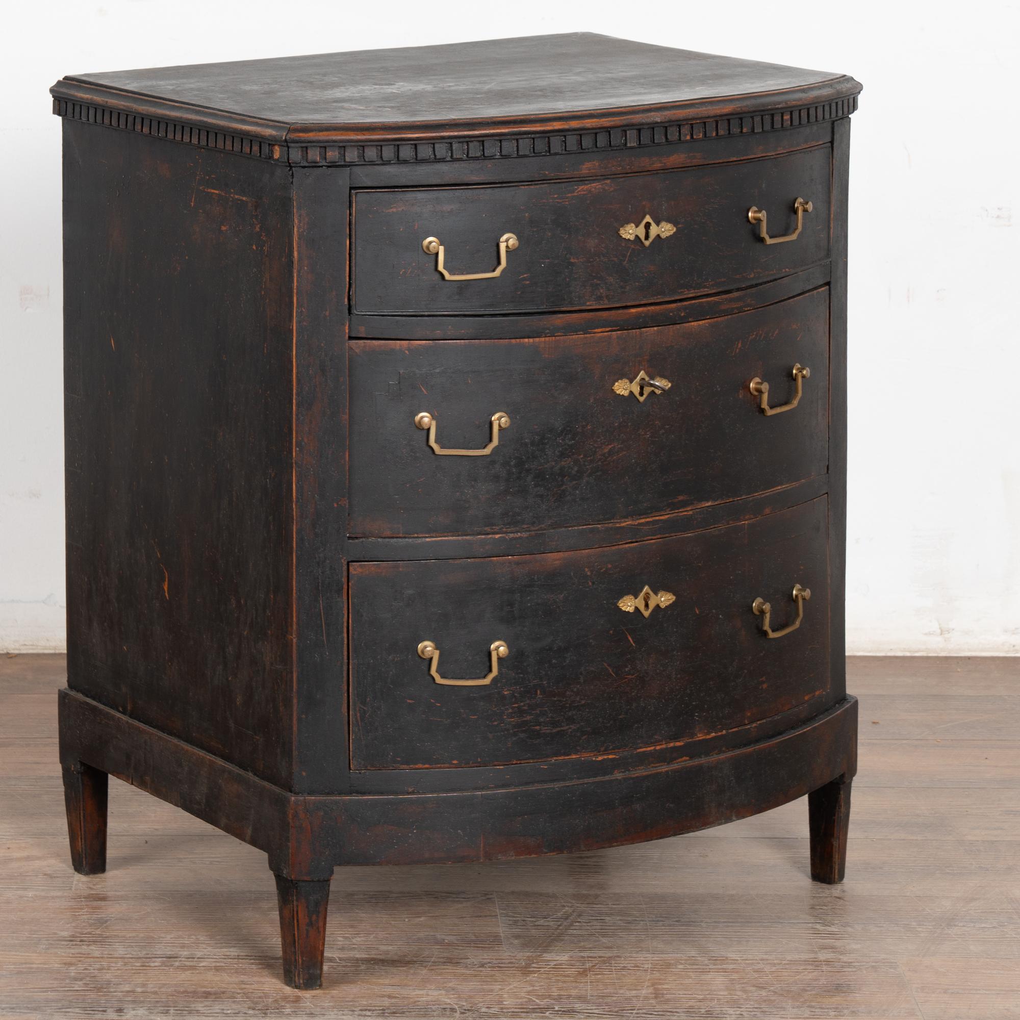 Cassettone in pino a tre cassetti con fronte ad arco, modanatura superiore a dentello che poggia su piedi affusolati, due tiretti in ottone su ogni cassetto.
Restaurata, successivamente dipinta professionalmente in tonalità stratificate di nero,