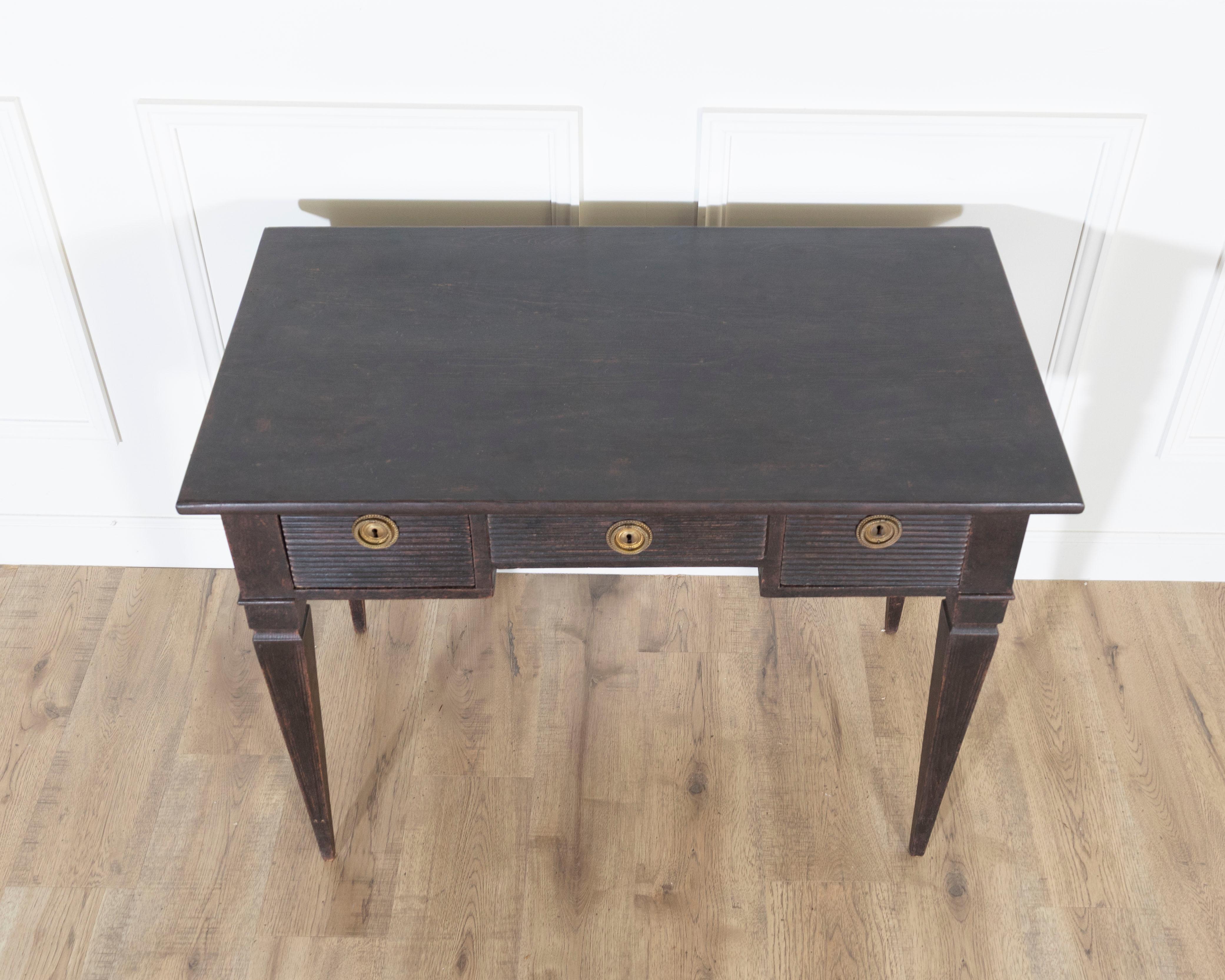 Elegant 19th-century Swedish writing desk in pine, finished in a rich black patina that highlights its refined Gustavian-inspired form. The desk features three drawers adorned with horizontal millings and fitted with original brass handles and