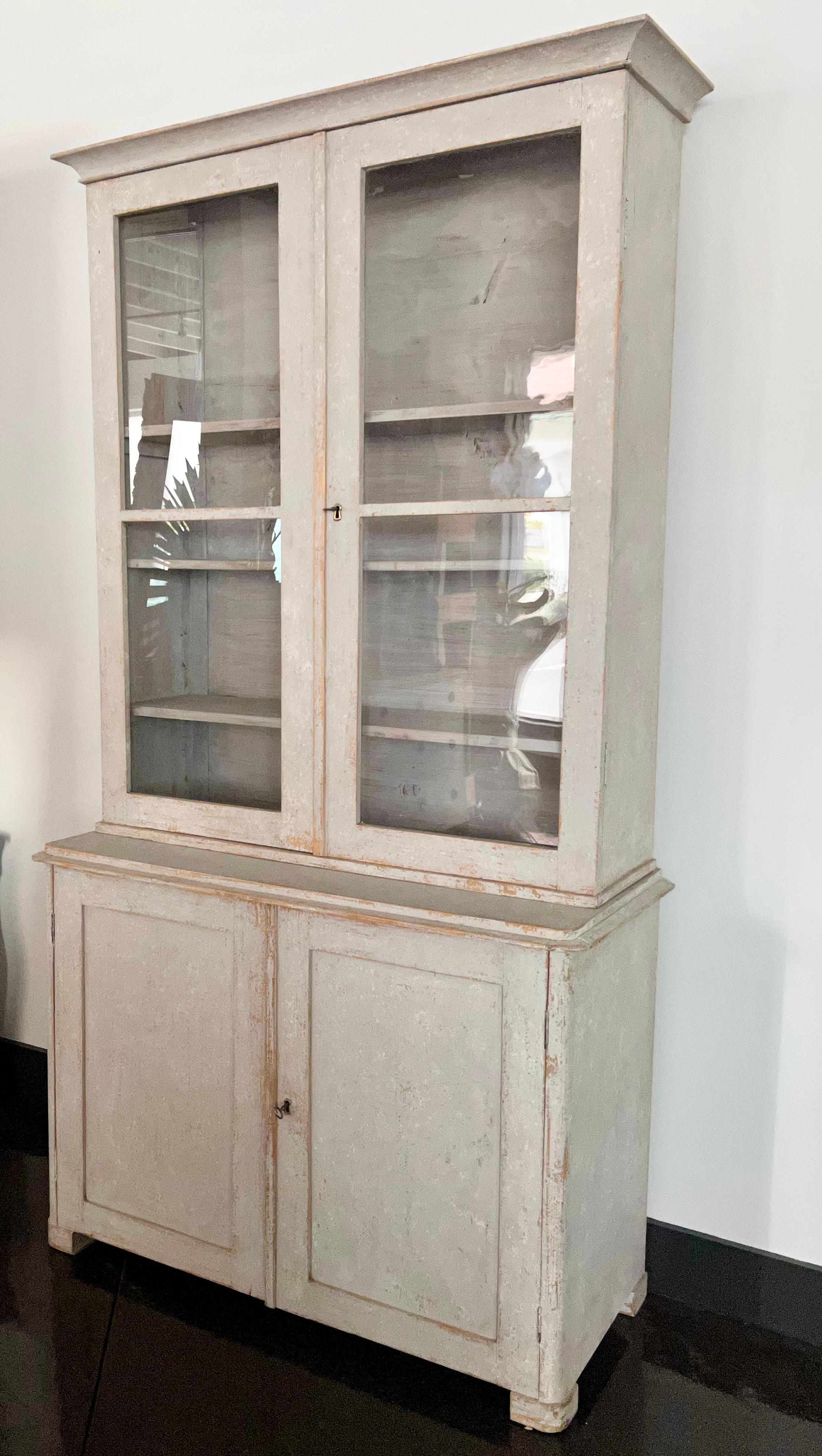 19th century Swedish bookcase / vitrine cabinet in two pieces with glass fronted doors in late simple Gustavian style.
Upper library section with molded cornice, three shelves behind double glass doors.
The lower cabinet with molded door fronts,