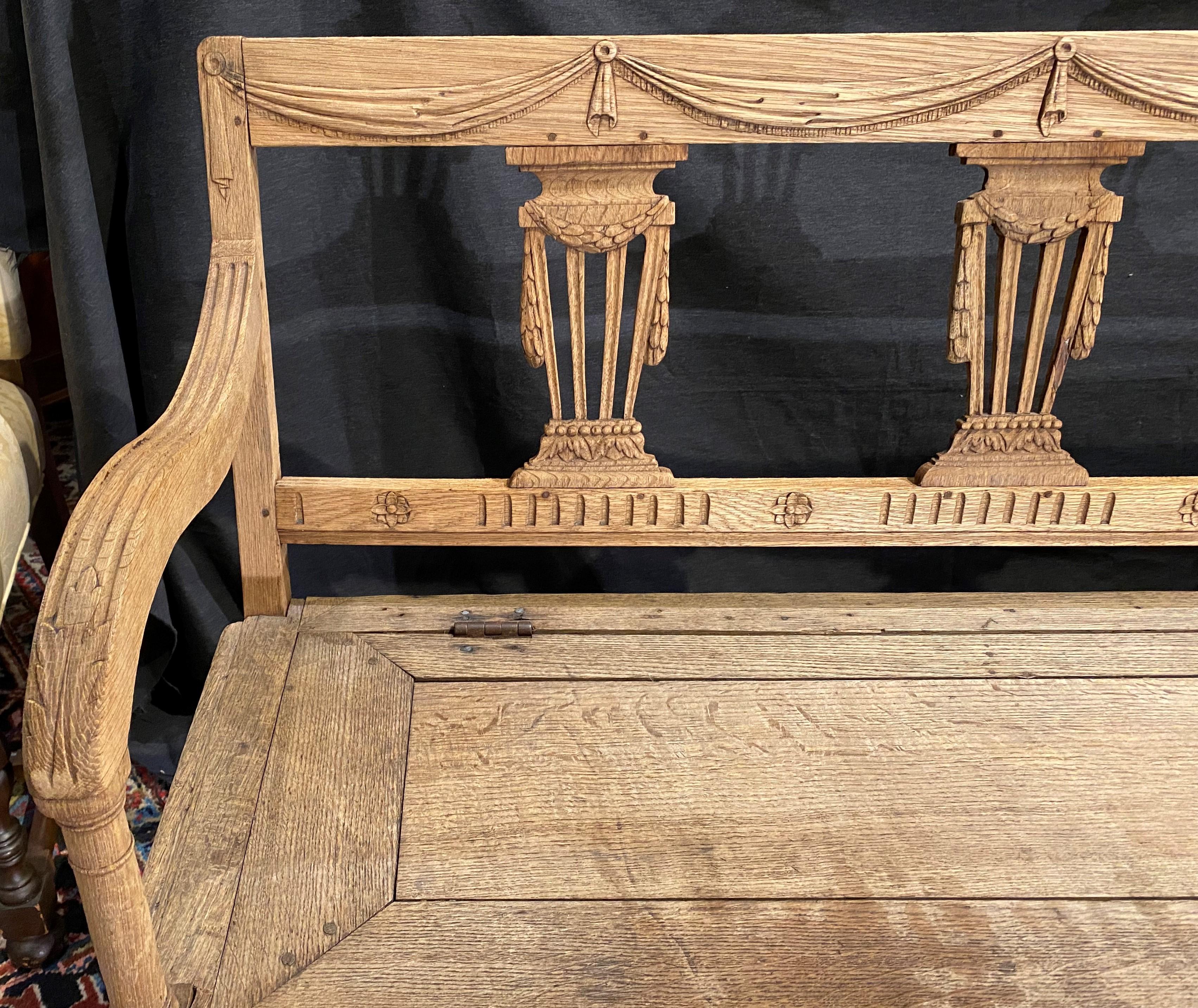 A fine solid Swedish hand carved bench or settee with a swag carved crest and pierce-carved pilaster splats decorated with swags across the back, scroll form arms, and a lift top bench seat over a storage compartment with four relief carved front