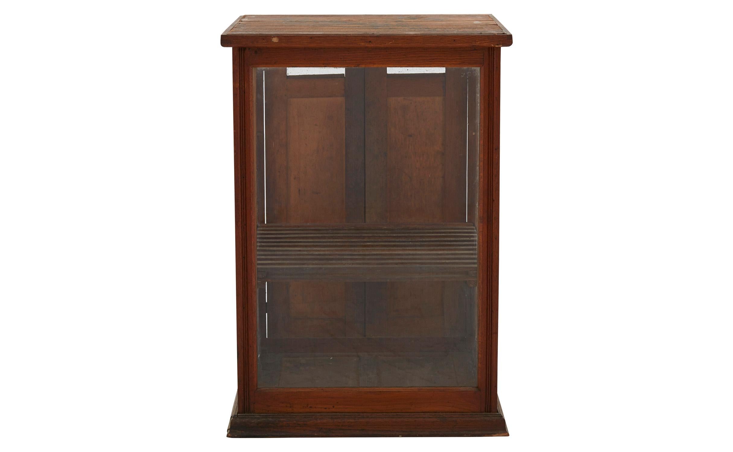 Our vintage shop display case was crafted in America in the early 20th century. Once used to exhibit small wares, this countertop case features a slatted wooden shelf, surrounded by three original glass sides and two wood hatch doors at its rear. It