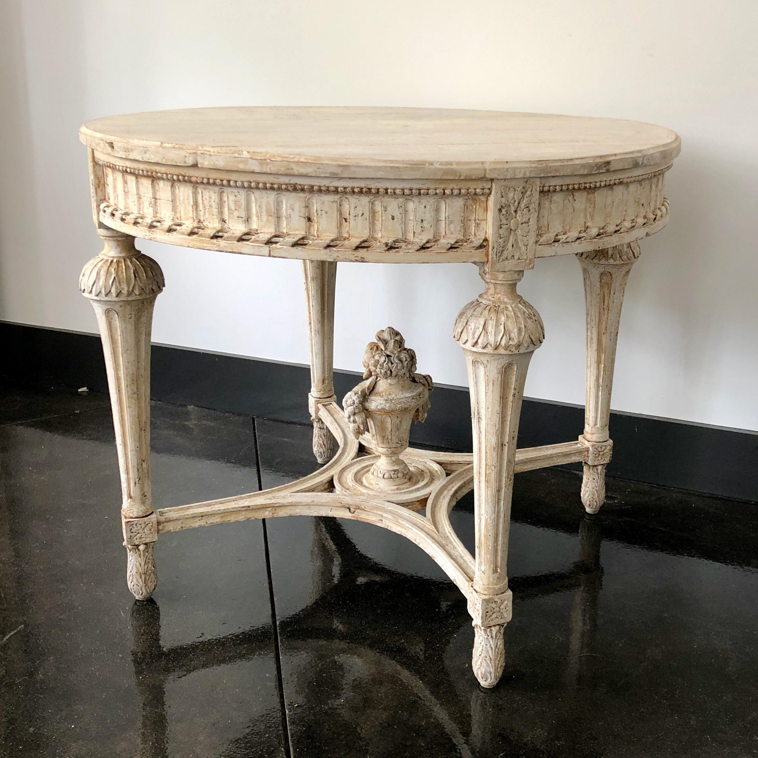 Swedish Gustavian style round center table with very richly carved apron, tapering carved legs and saltire strecher with central medallion in painted worn cream patina, Sweden, circa 1860.