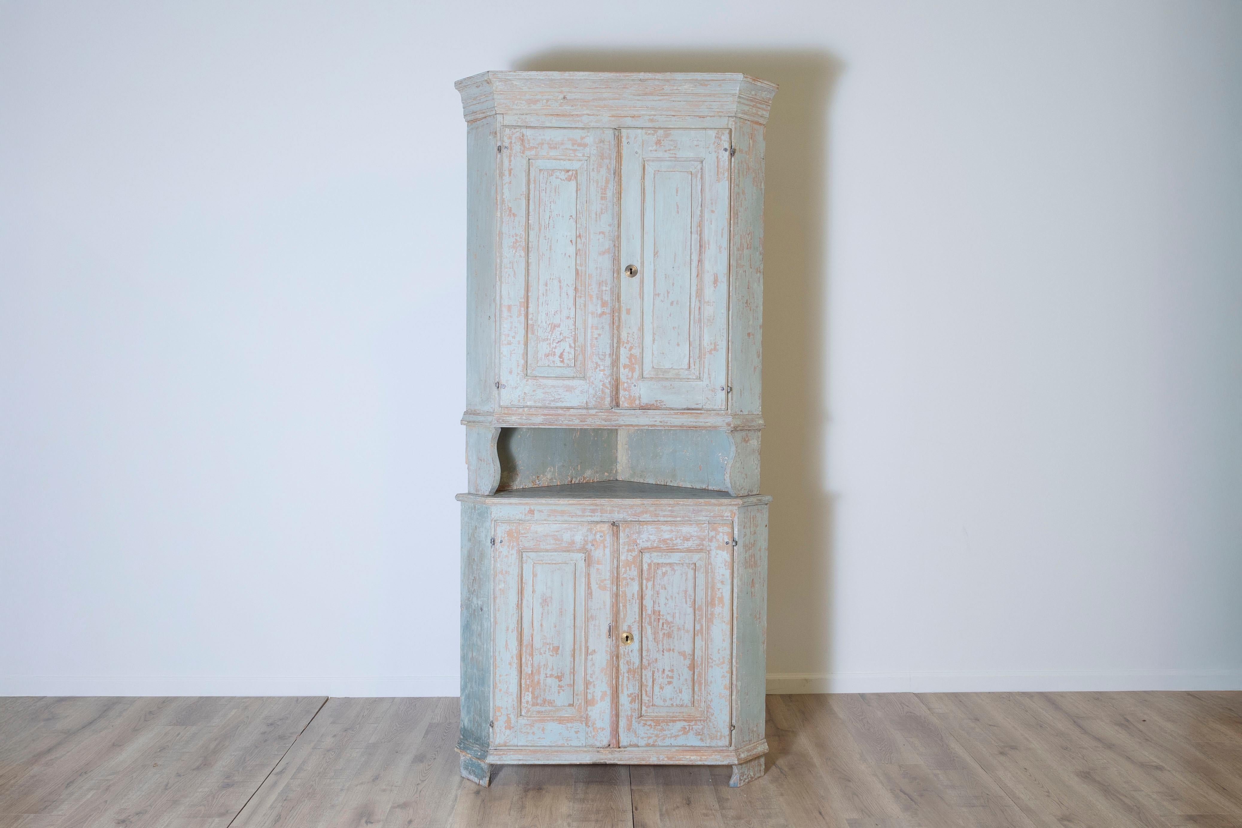 Questo armadio angolare svedese dei primi del XIX secolo, proveniente da Ångermanland, è un notevole esempio di artigianato scandinavo di provincia. Raschiato per rivelare l'originale finitura grigio-verde, il pezzo mostra una patina autentica e