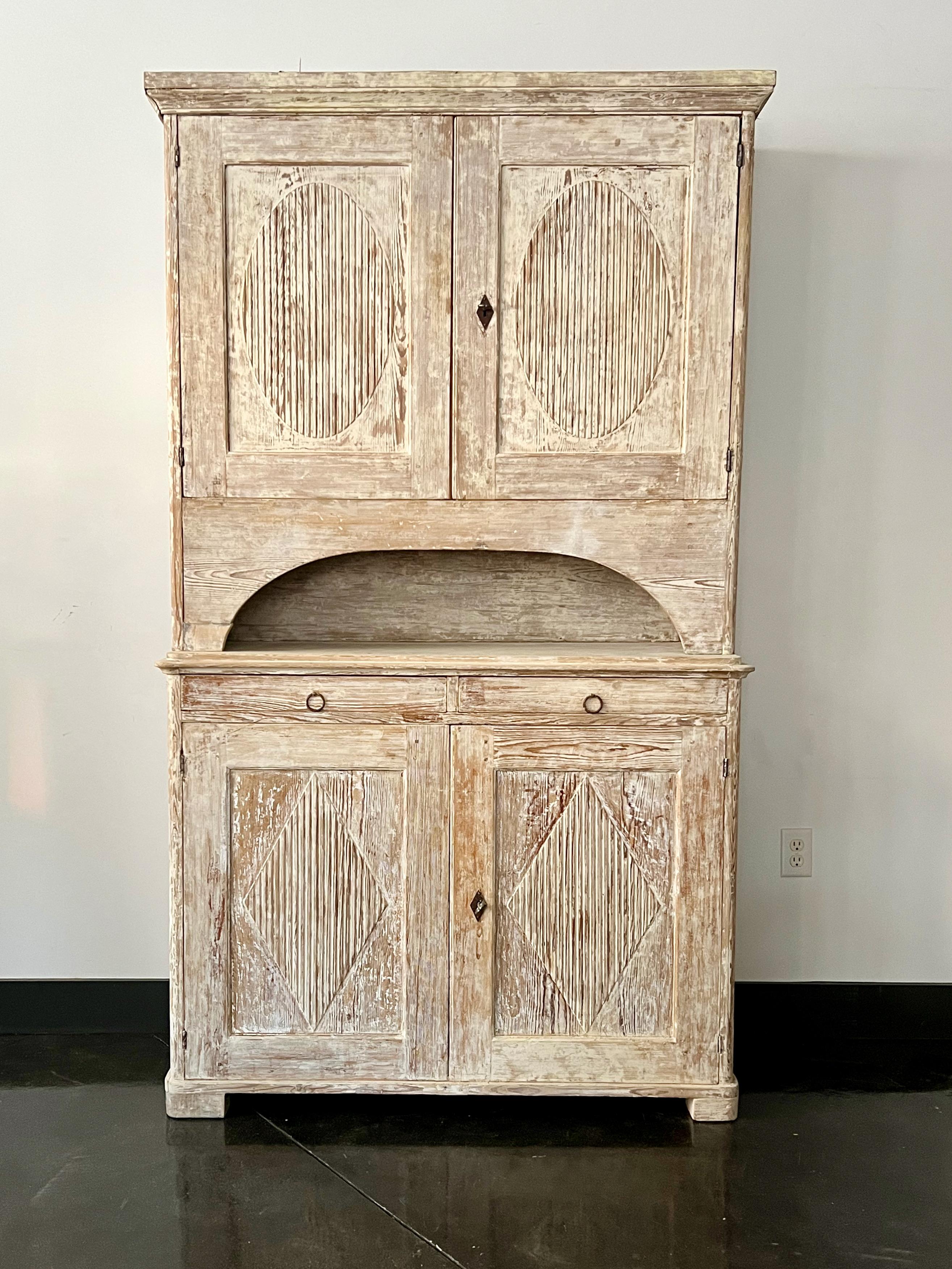 19th century Swedish cabinet in two parts displays classic Gustavian styling with reeded, shaped decor door panels in worn cream white patina scraped back to most its original finish.
Supported the sturdy two-door base with block feet.
 Very