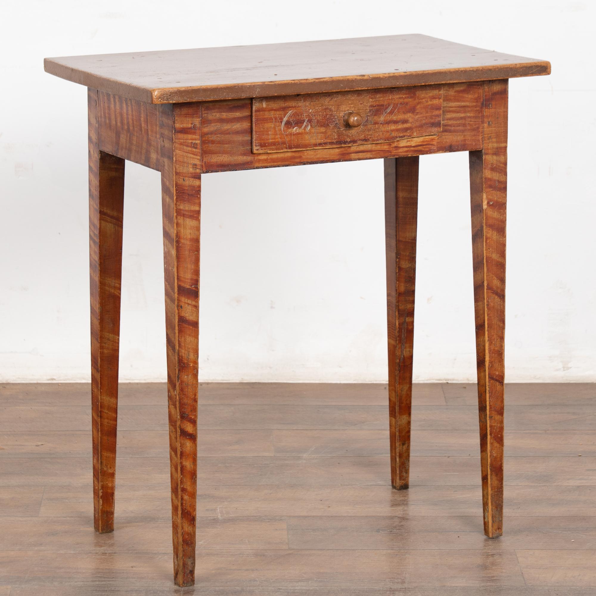 This delightful pine side table comes from the Swedish countryside and still maintains the original faux wood painted finish with contrasting brown top.
The single drawer has the faint remains of a monogram which indicates it may have served as a