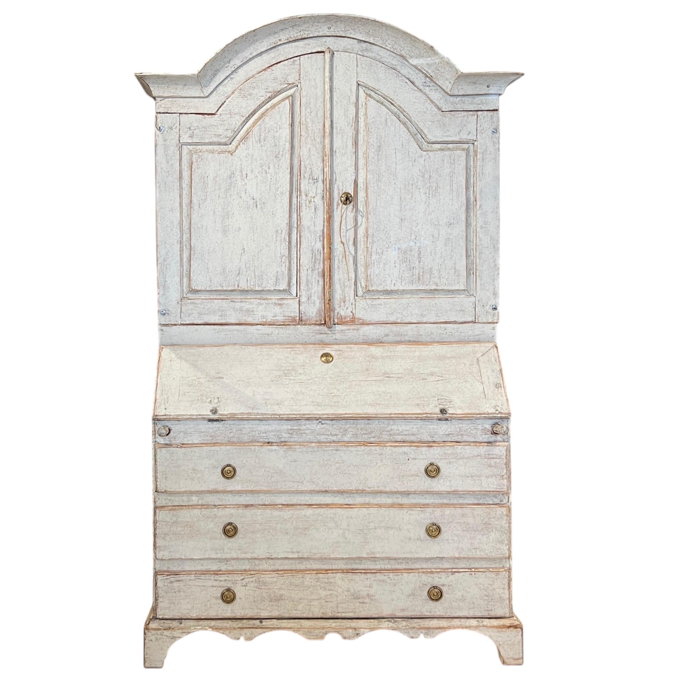 Un majestuoso secreter de estilo Gustaviano con una refinada silueta neoclásica, puertas paneladas, escritorio abatible y seis cajones. La pieza tiene un acabado pintado suave y apagado, que combina la elegante artesanía sueca con la sofisticación