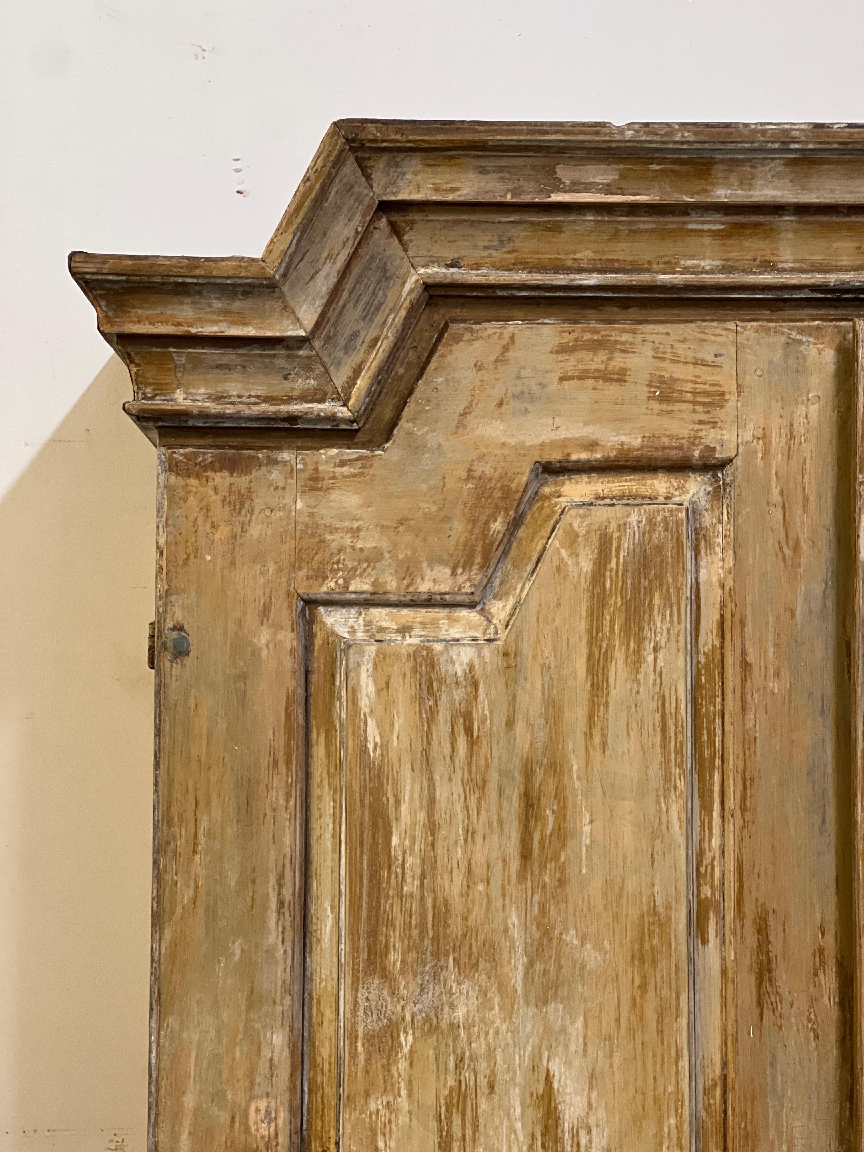 A beautiful Swedish Gustavian cabinet that has been painted and dry scrapped over its lifetime. It dissembles into two parts. This beautiful piece shows the original paint job with painted details underneath the layers and has a scalloped bottom.