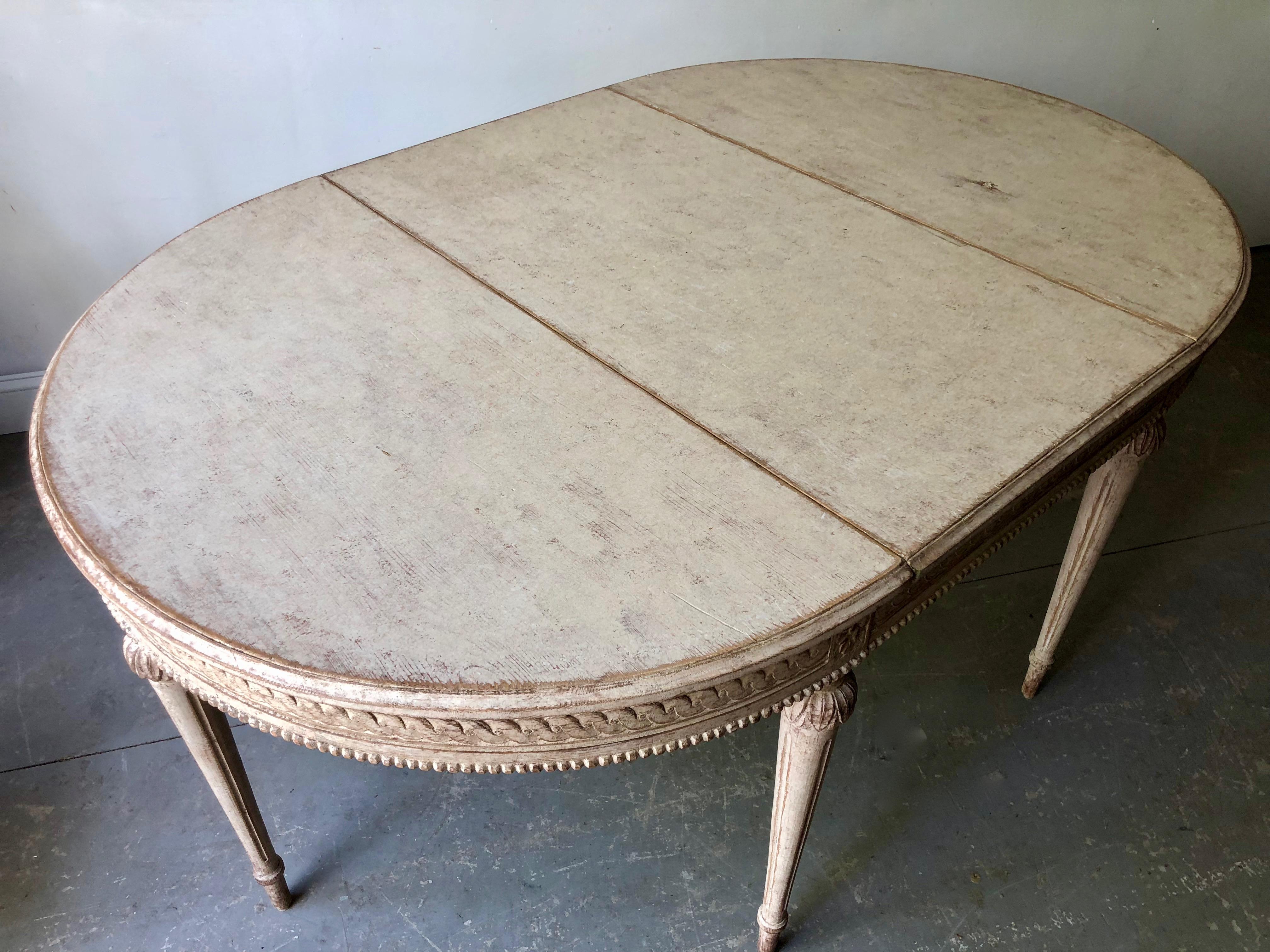 19th century painted Gustavian extending table with original leaf and very richly carved apron and tapered legs. A practical piece that can be used as round table, console tables or extended with one leaf up to 65