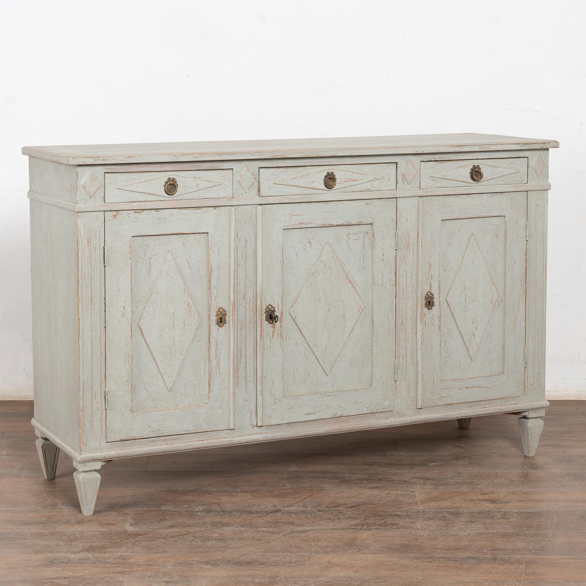 Swedish Gustavian gray painted pine sideboard or buffet console resting on tapered fee.
Traditional diamonds accent the three drawers and three doors. Keys and locks still function or can be used as pulls. 2 keys included.
The newer, professionally