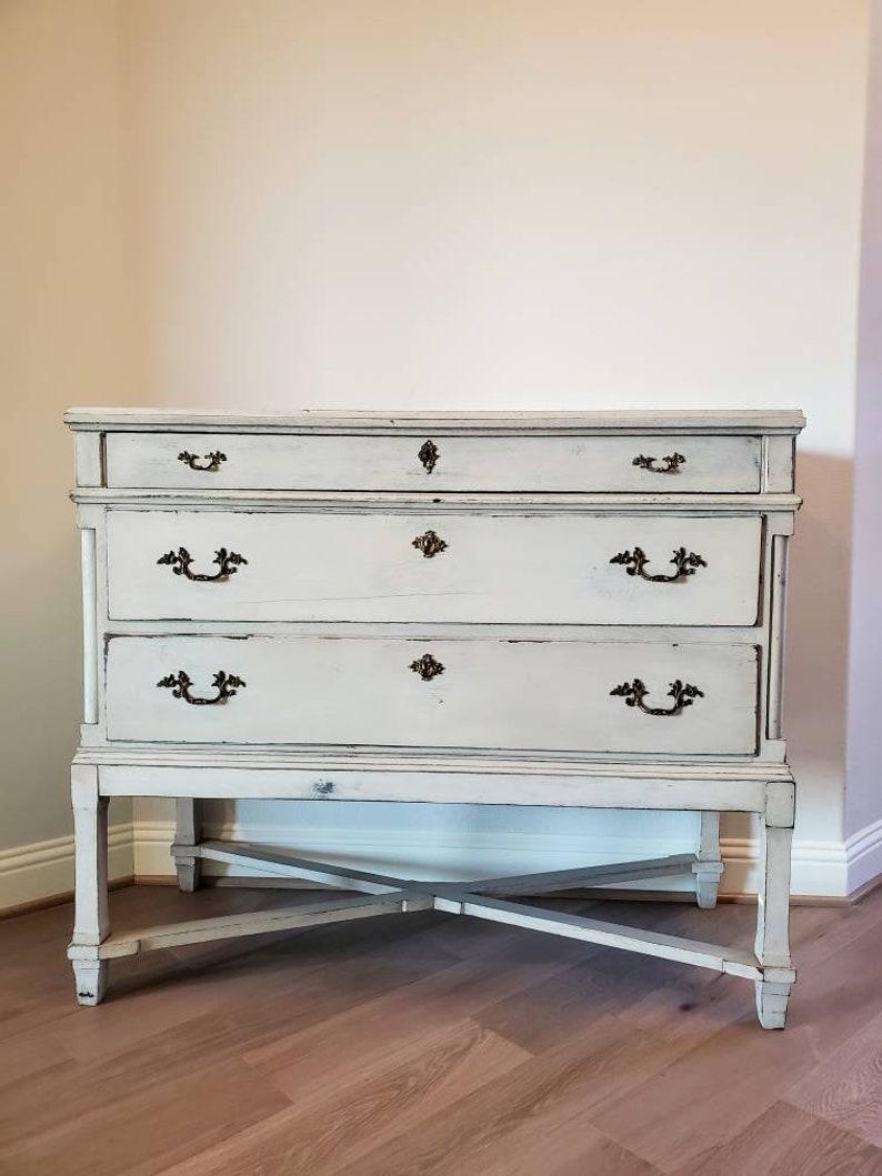 A Swedish Gustavian style chest of three drawers. Born in Sweden during the early 19th century, finished in Neoclassical taste, the finely hand-crafted antique solid pine wooden chest painted in a soft gray/white color, typical of Scandinavian