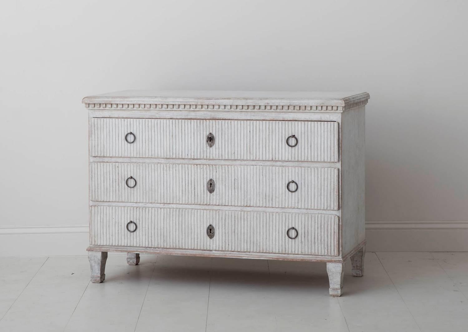 A charming late Gustavian period commode with reeded drawer fronts and dental molding framing the top. Original locks and hardware. The patina is a complex blend of aged white and soft gray with natural wood showing through in some areas.