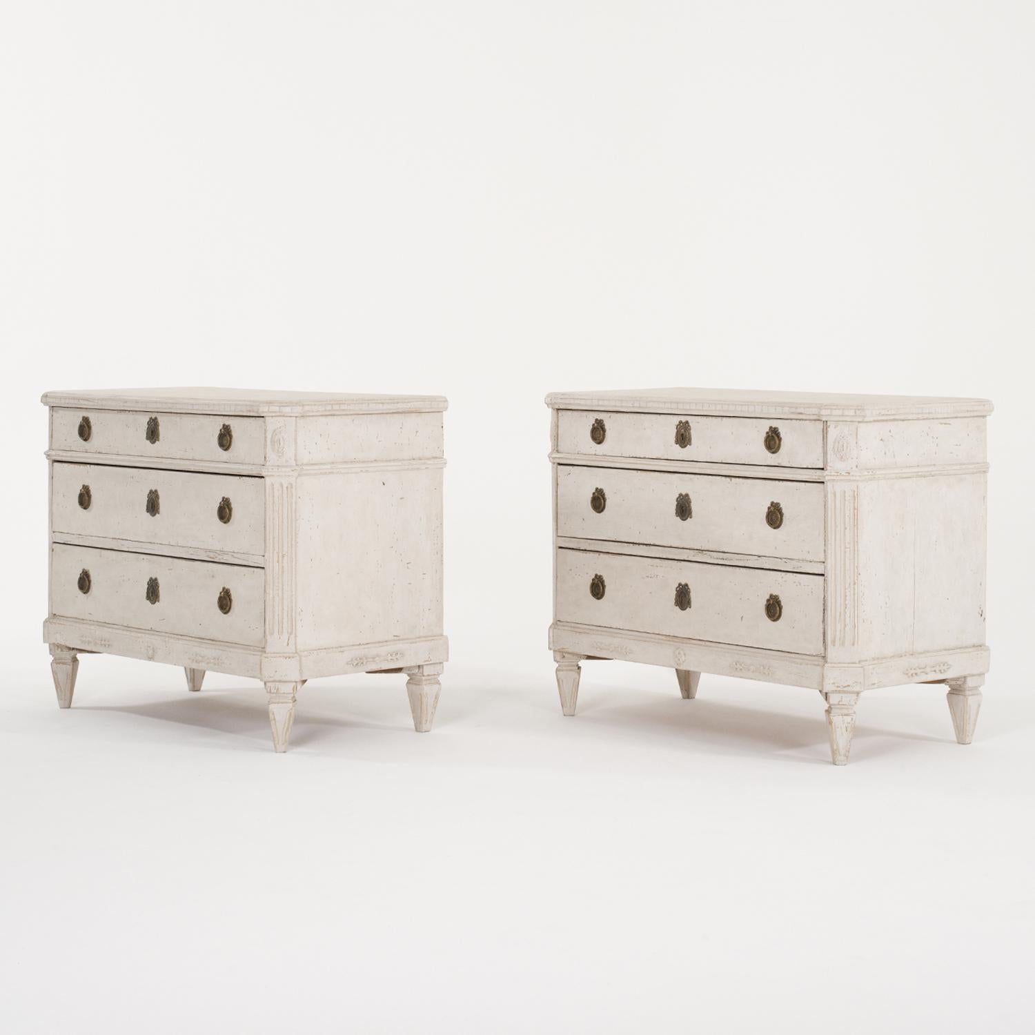 A 19th Century, light-grey antique Swedish Gustavian pair of chests made of hand crafted painted Pinewood with two large drawers and one small one, in good condition. The Scandinavian cabinets are enhanced by detailed wood carvings, standing on four