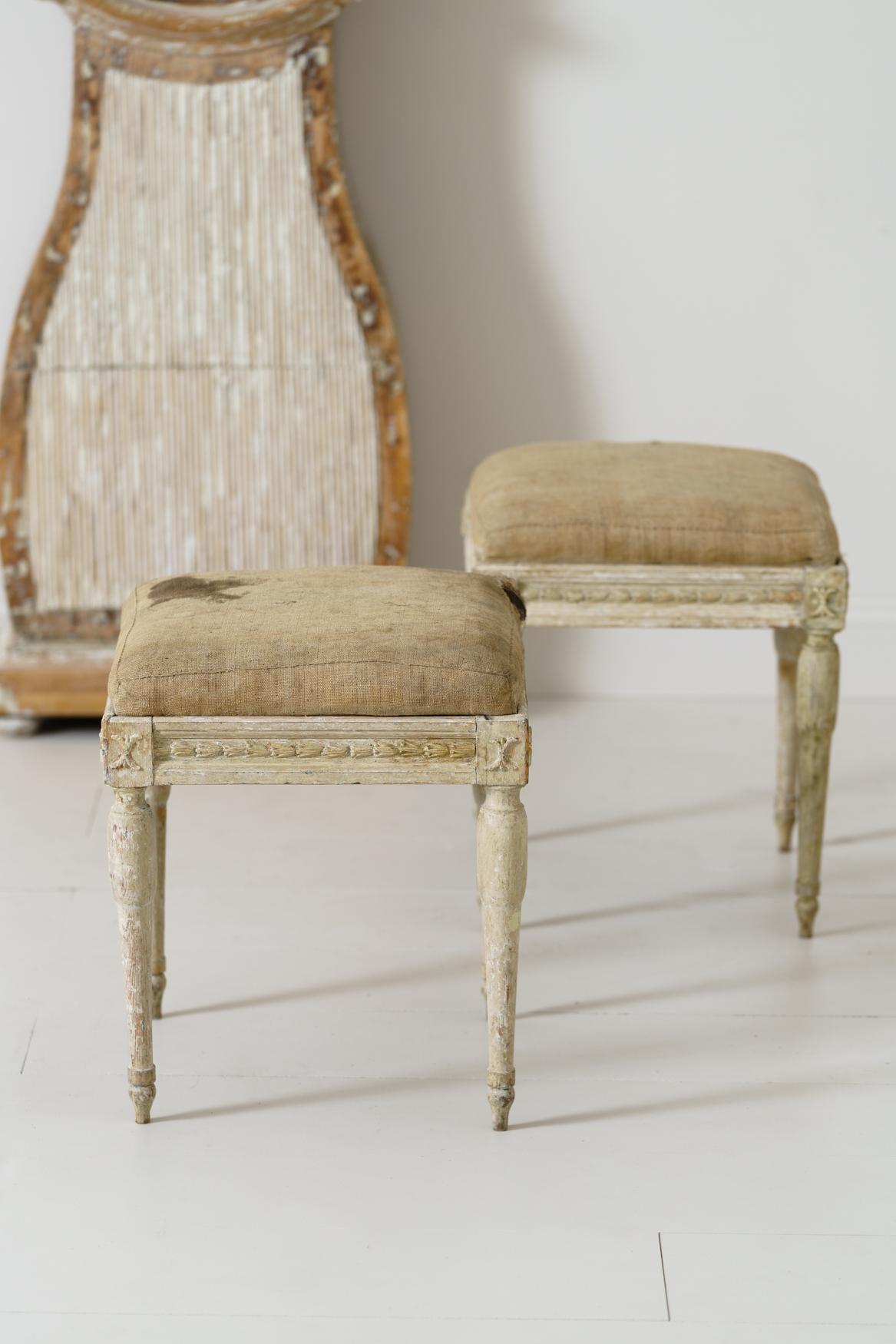 A pair of Swedish period Gustavian stools from the 19th century wearing their original linen. There are carved bell flowers on the seat frame with wheat sheaths on the corner posts. Manor house quality stools.