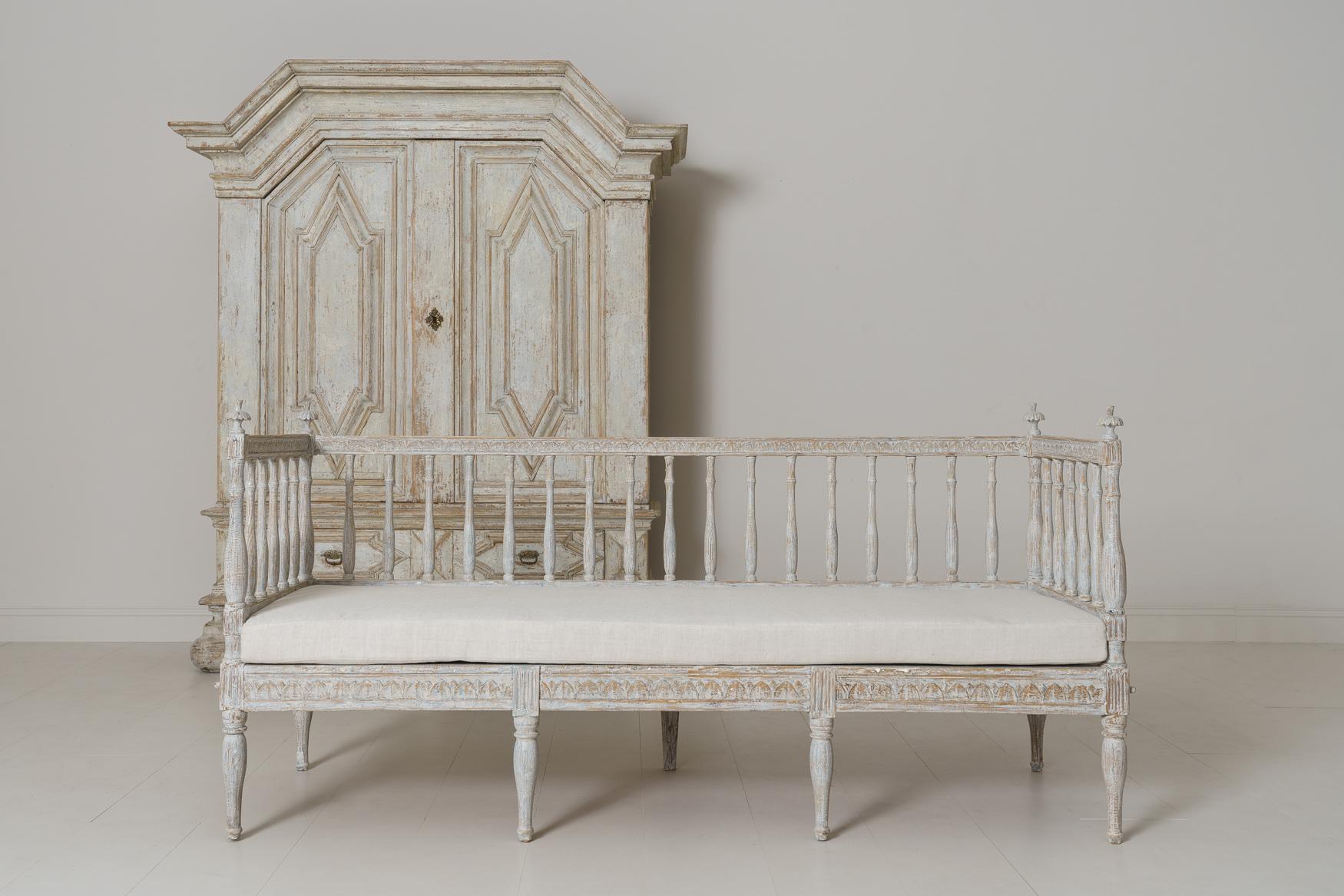 A Swedish Gustavian period sofa bench from the 19th century with a soft blue and aged white painted patina, newly upholstered in linen, circa 1800. Baluster back and sides with turned finials. The seat and back feature carved egg and dart detail.