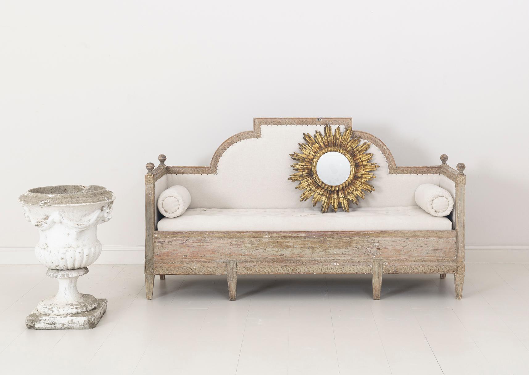 A beautifully carved Swedish sofa bench from the Gustavian period, hand-scraped to reveal the original paint surface and newly upholstered in linen with a hand-stitched tufted seat and side bolster pillows, circa 1800. The back and seat frame