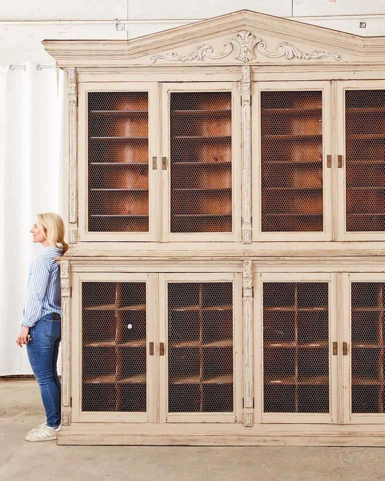 Grand 19th century Swedish Gustavian style library bibliotheque two-part bookcase cabinet crafted from pine. The upper case features a large corniced gable roof decorated with acanthus scrolls. Fronted by four large doors with chicken wire windows