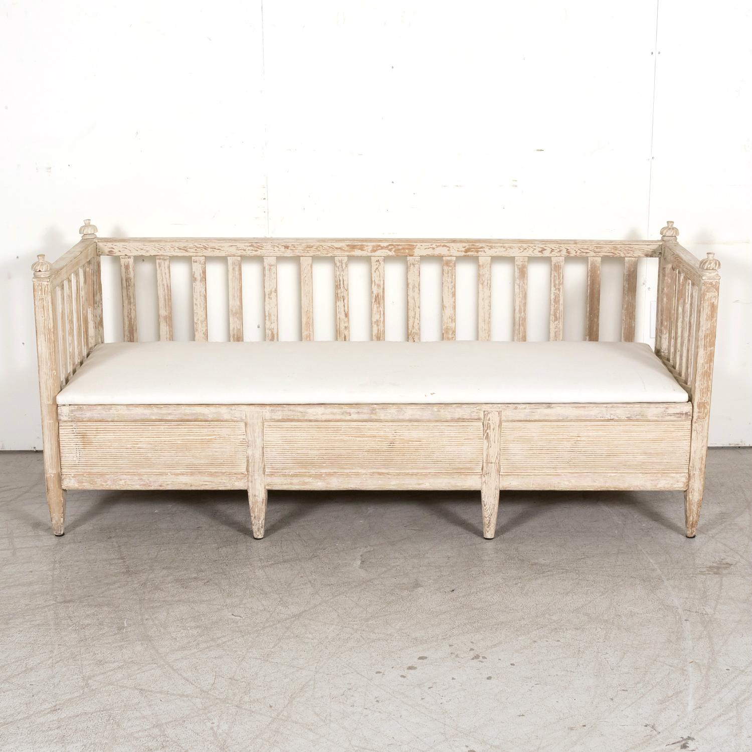 A mid-19th century Swedish Gustavian style painted wood stick back kitchen sofa or bench, circa 1850s. Scraped to the original off white paint, this antique sofa bench is typical of the Swedish desire for light and soft colors that helped bring