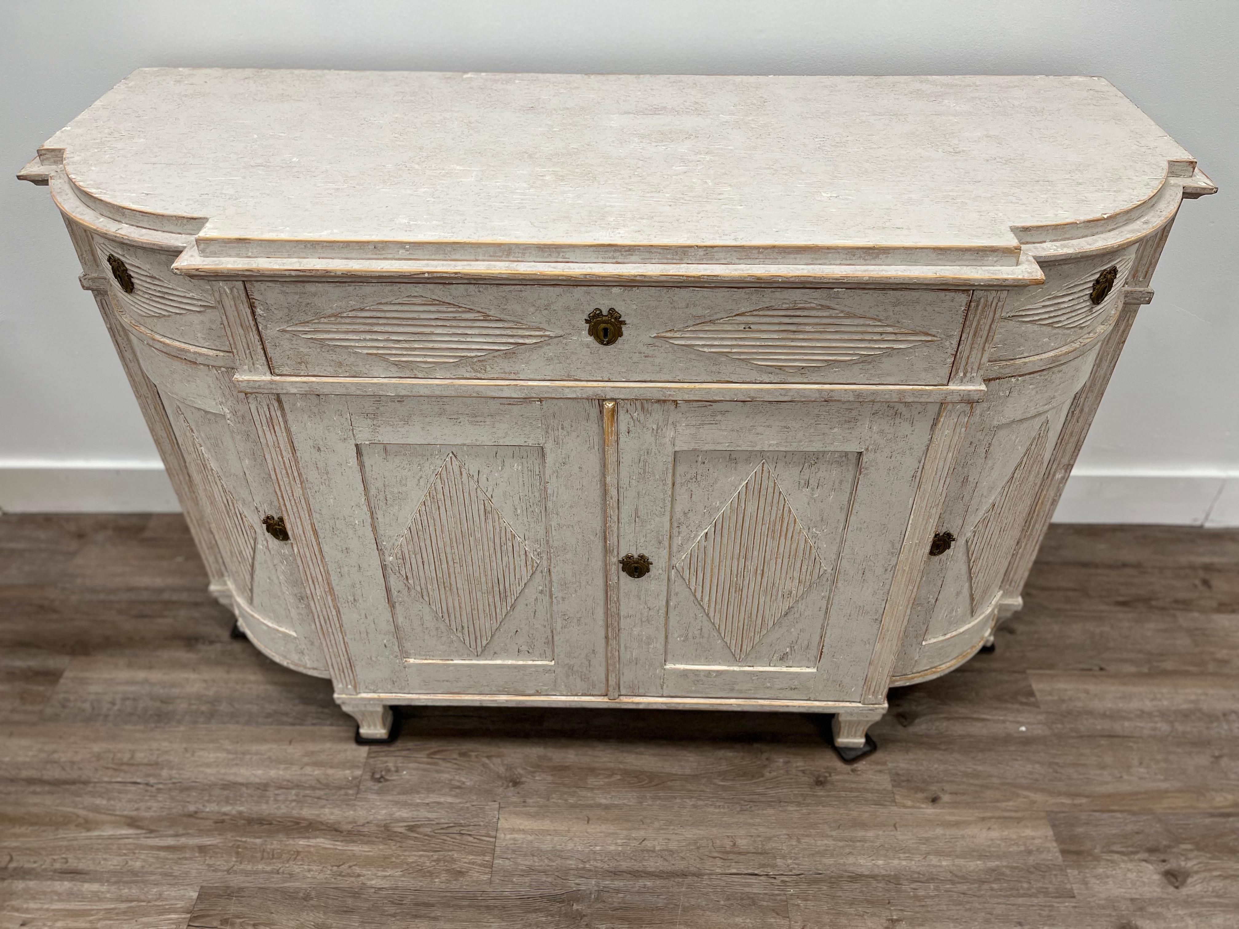 A long Gustavian style sideboard with original brass hardware and locks. Featuring a raised top and curved corners with horizontal diamond-shaped reed detail on the drawer fronts and vertical diamond-shaped reed detail on the door fronts. Behind the
