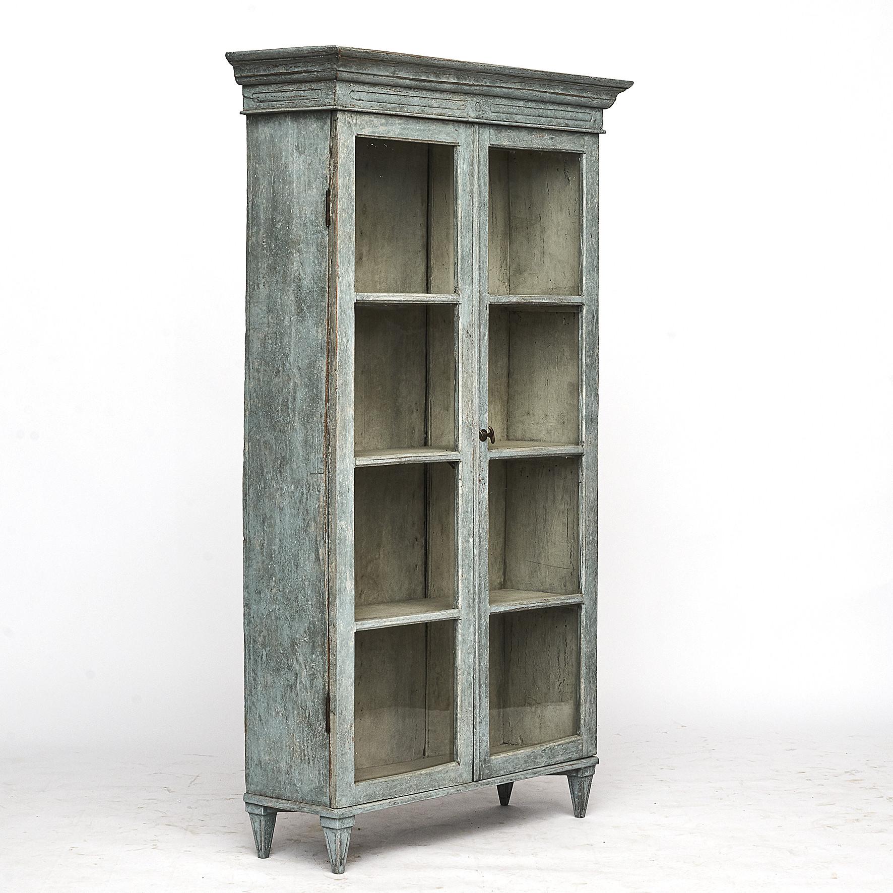 Swedish Gustavian style cabinet with a pair of paned glass doors resting on four fluted tapering legs. Closure of the doors in the form of the handle.
Later professionally antique repainted in a blue color with a grey-white interior.
Sweden