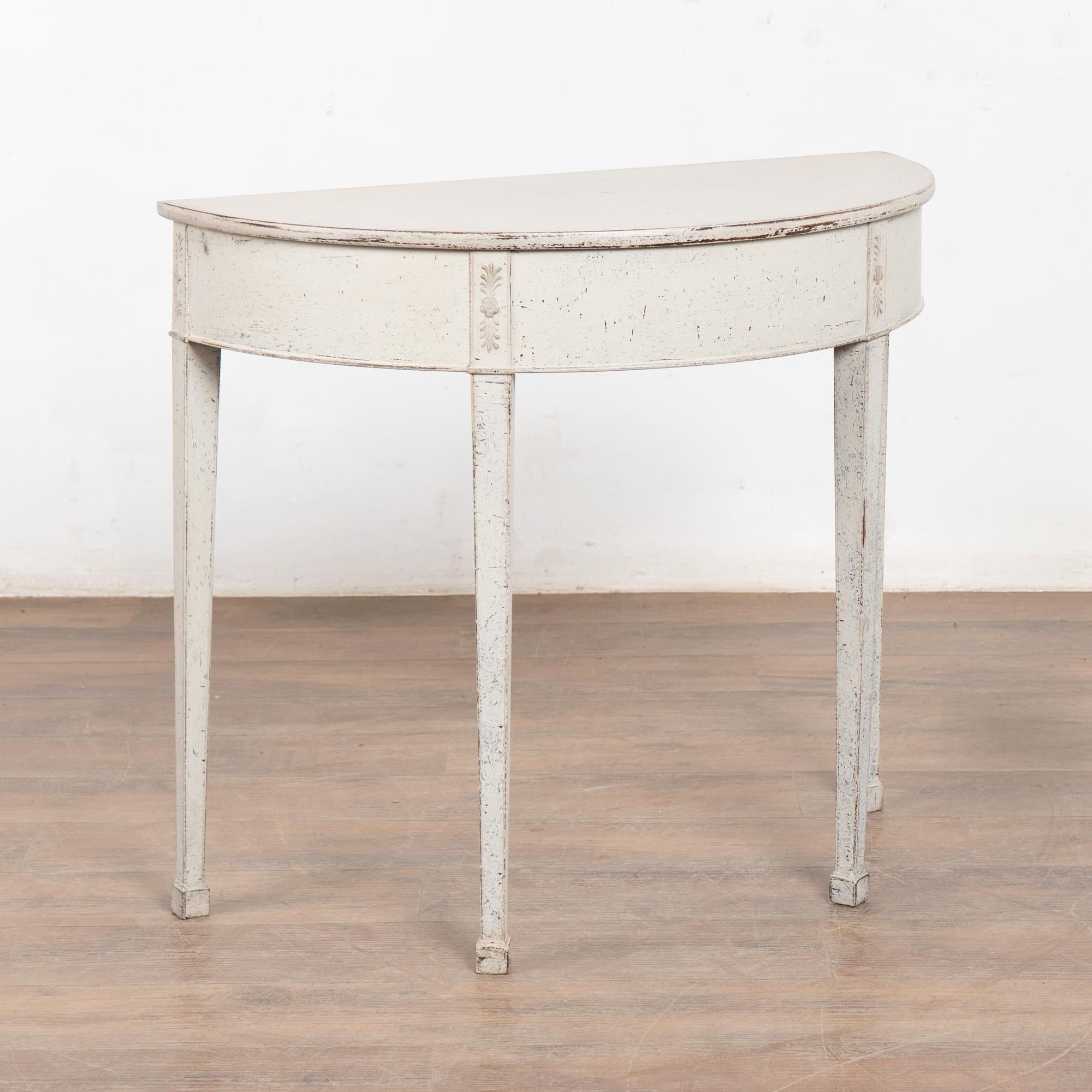 Swedish Gustavian single demi-lune pine side table or console with gently tapered fluted legs and decorative applied carving along skirt.
Newer professionally applied layered antique white painted finish, slightly distressed to fit age and grace of