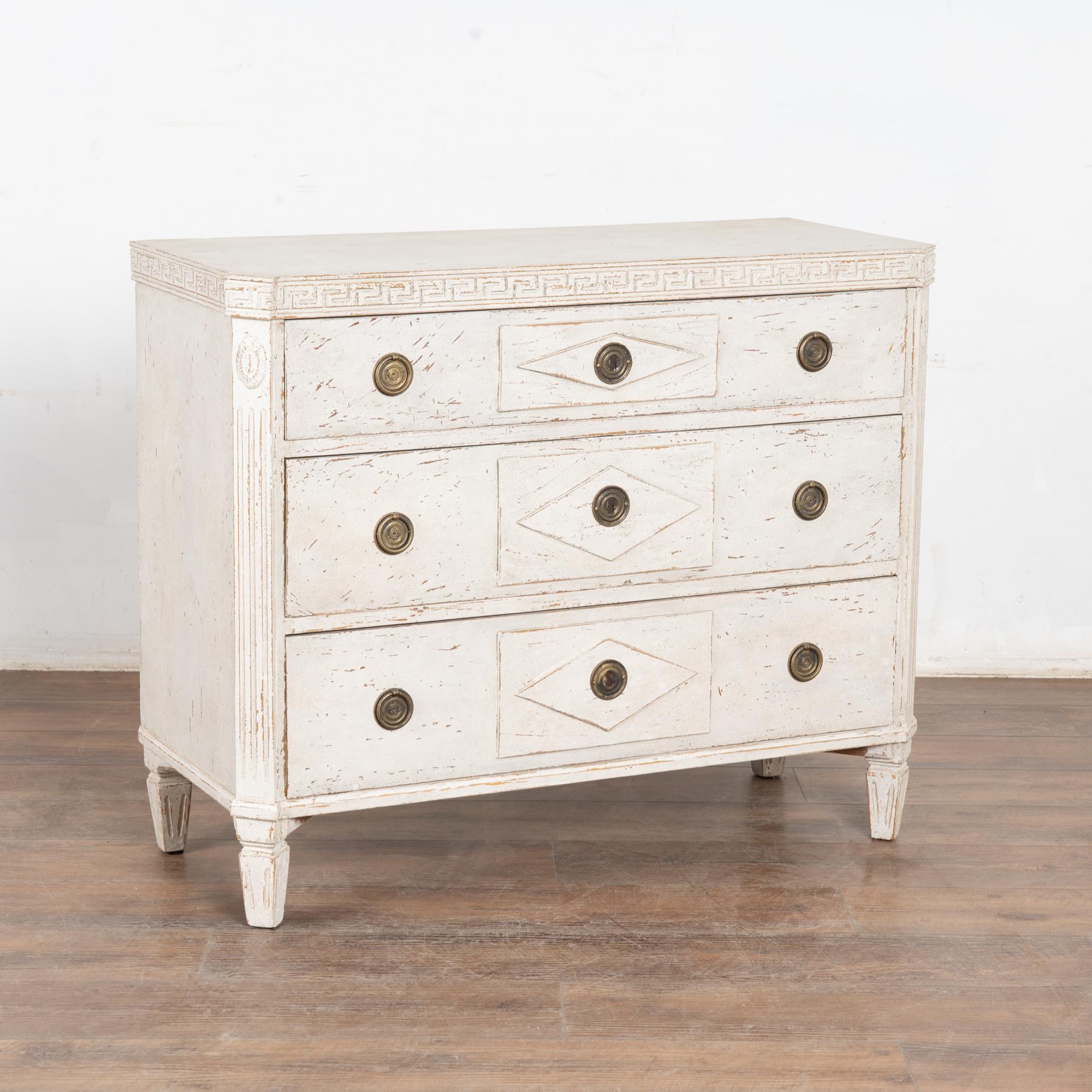 Lovely Gustavian pine chest of three drawers with diamond accent on drawers, fluted canted sides, Greek key motif and tapered fluted feet.
The newer, professionally applied layered white painted finish (undertones of soft gray) is gently distressed