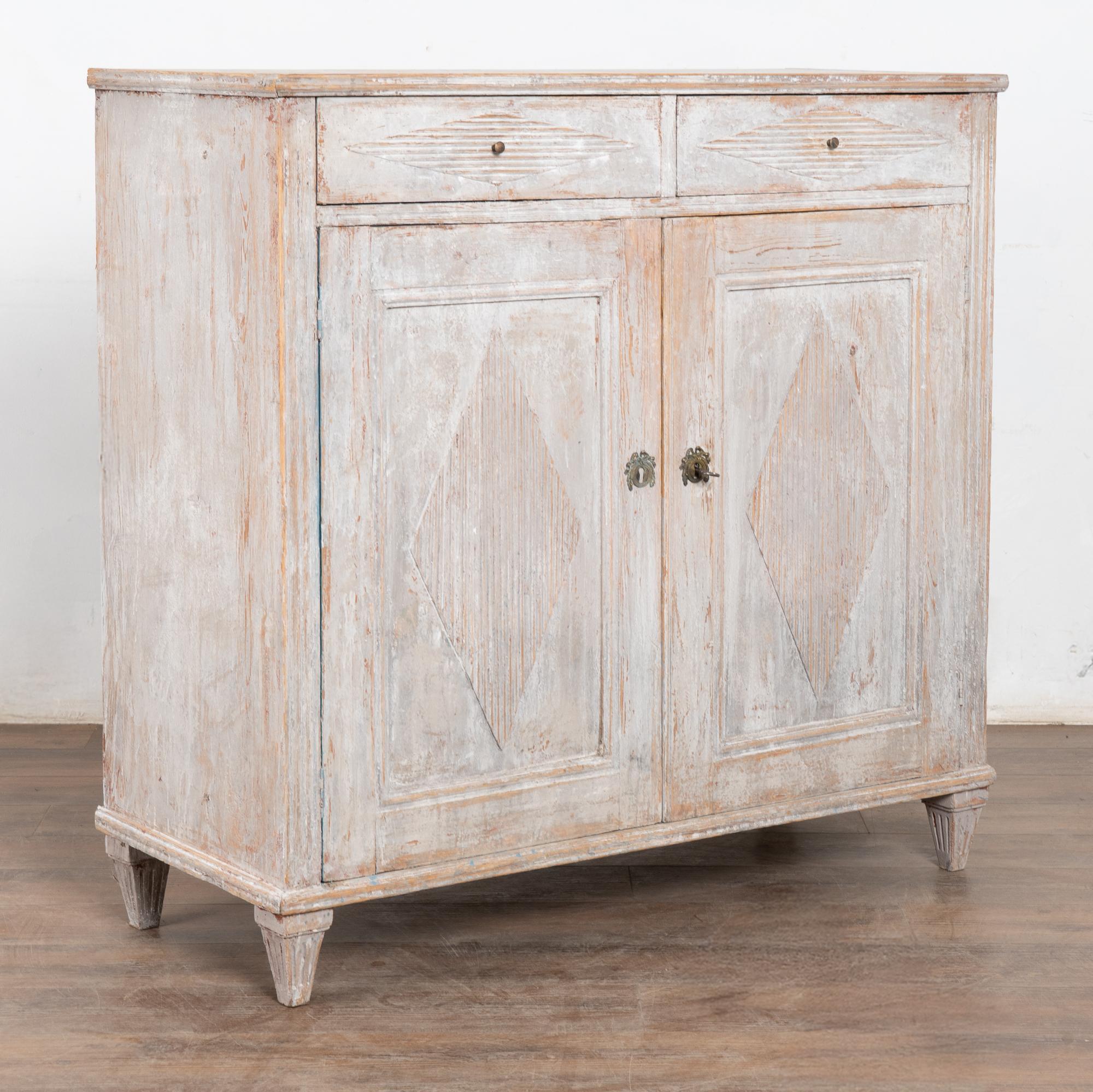 Gustavian pine sideboard or buffet with traditional decorative fluted diamond panels on cabinet doors. 
Later painted in layered shades of antique white with gray undertones and lightly scraped and distressed to fit the age and grace of this Swedish