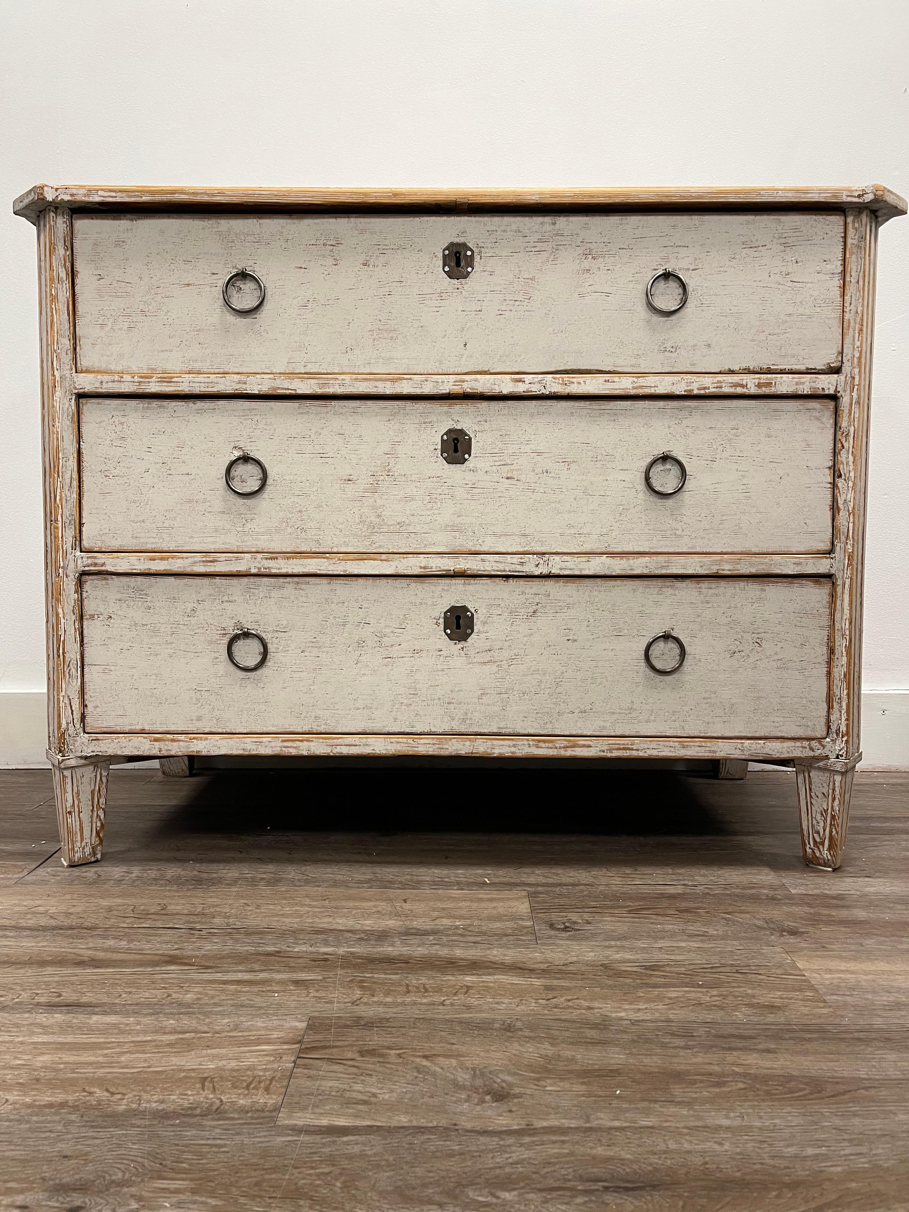 A three drawer Swedish Late Gustavian commode. Front corners are canted and fluted. Back corners are fluted as well. Sits atop tapered rectangular feet. Later iron pulls and original iron locks. Repainted in soft grey. 