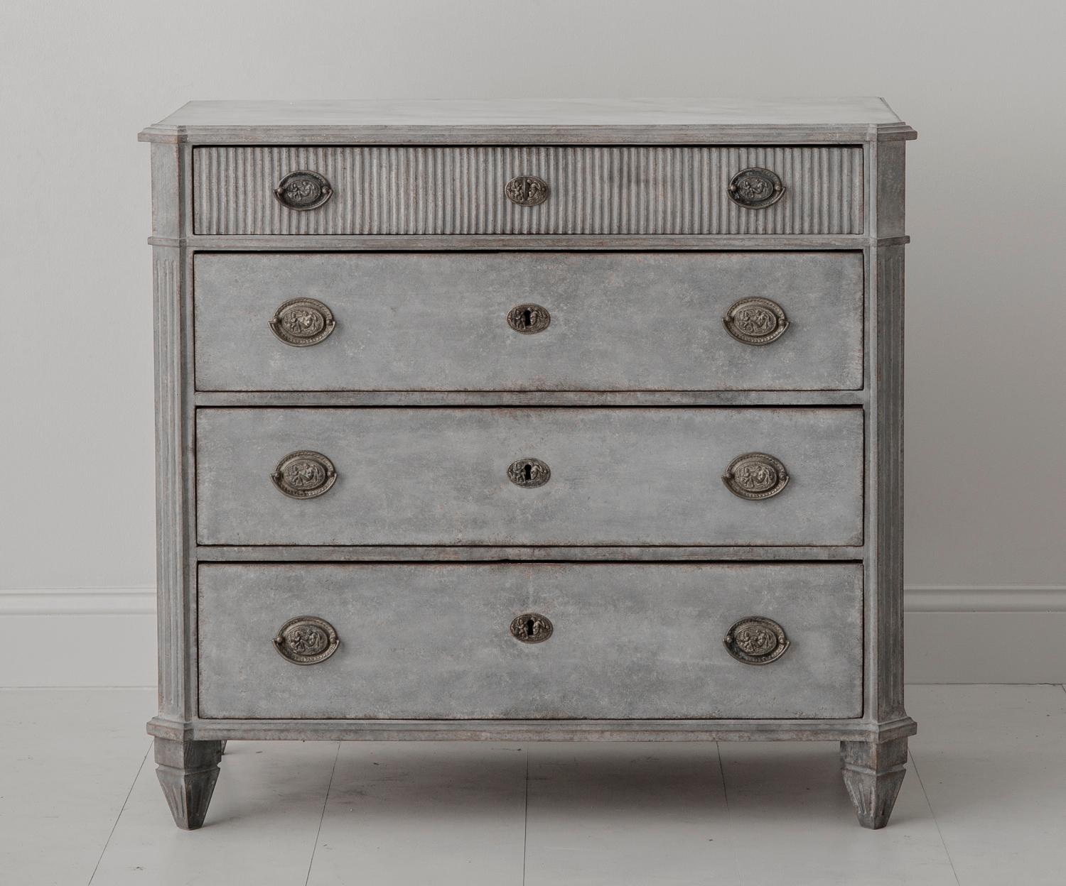 A handsome, neoclassical chest in the Gustavian style with a hand-painted marbleized top. The patina is mix of light blue and grey. There are four drawers, the top fully reeded, with brass hardware. The corners are canted and fluted and the chest is
