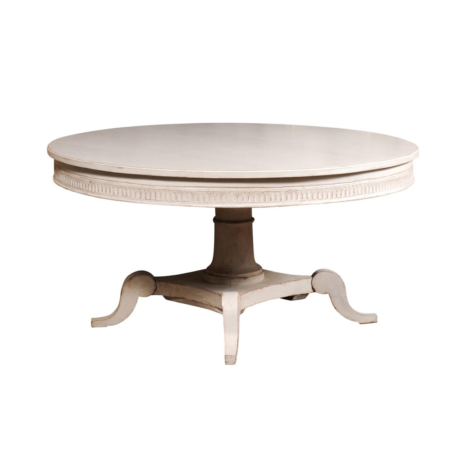A Swedish round top dining table from the 19th century with classic light gray painted finish, carved frieze, pedestal and carved quadripod base. From the heart of 19th-century Scandinavia comes this exquisitely designed Swedish round-top dining