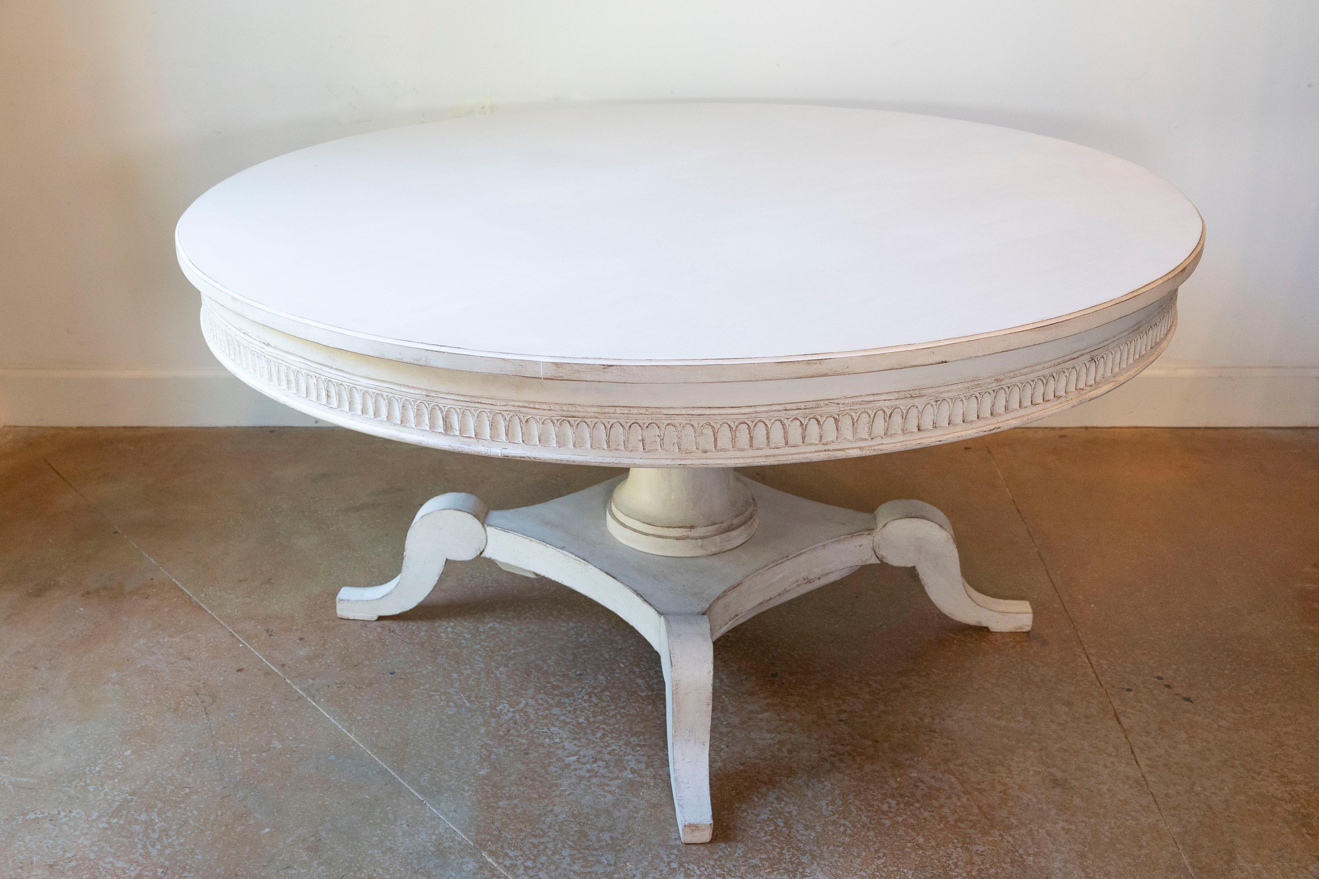 A Swedish round top dining table from the 19th century with classic light gray painted finish, carved frieze, pedestal and carved quadripod base. From the heart of 19th-century Scandinavia comes this exquisitely designed Swedish round-top dining