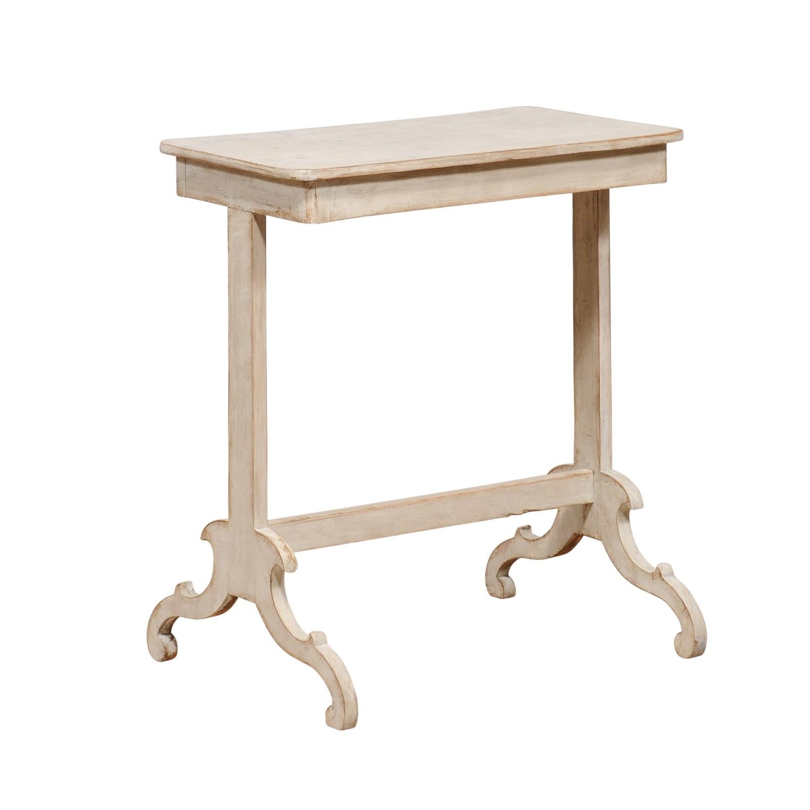 A Swedish side table from the 19th century with light gray painted finish and carved trestle base. Unveil the understated elegance of this 19th-century Swedish side table, a genuine antique treasure that whispers tales of yore. Coated in a serene