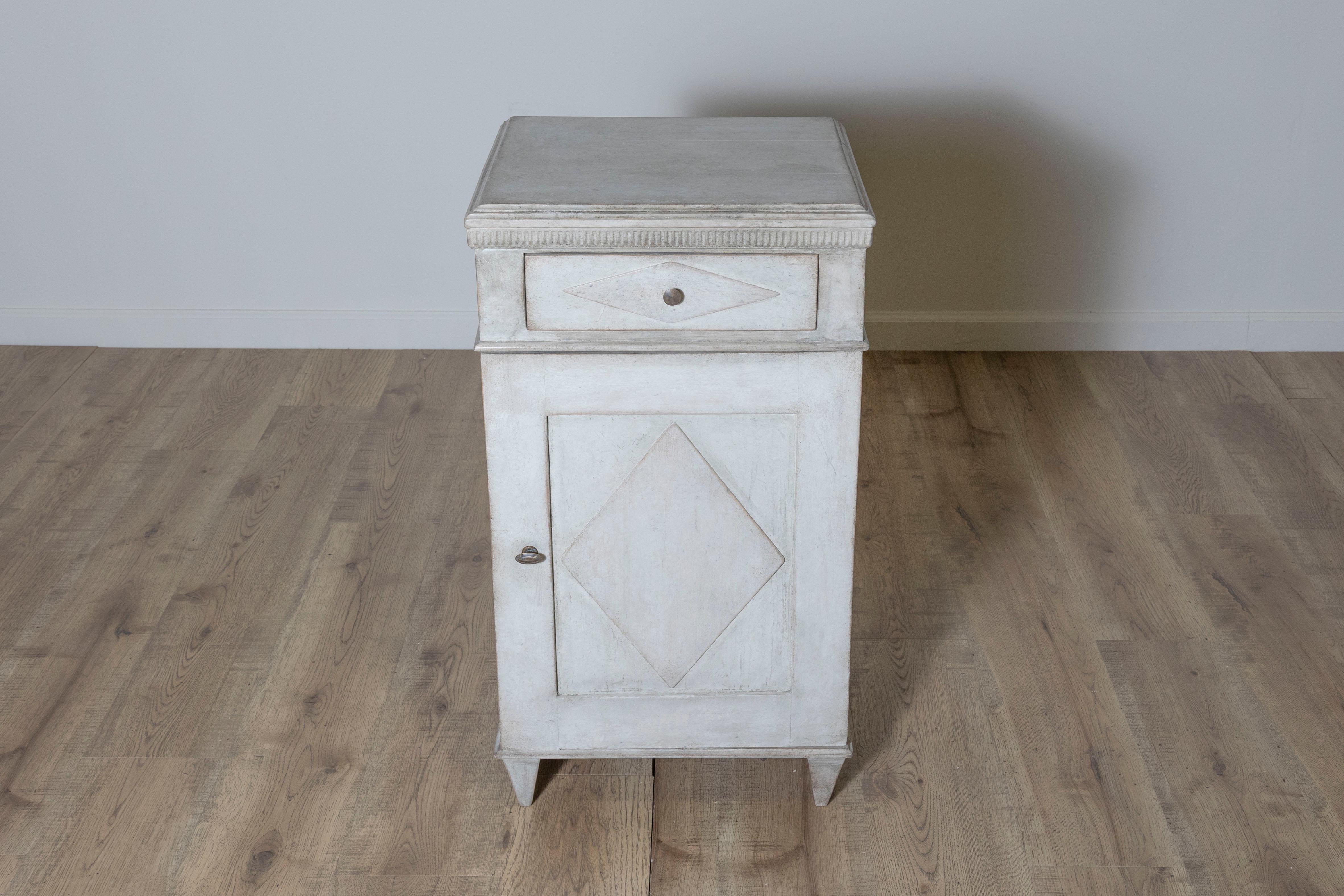 Cette charmante table de chevet suédoise du XIXe siècle allie la fonctionnalité à l'élégance intemporelle du design gustavien. Fabriqué en bois de pin, il présente une finition peinte grise légèrement vieillie, créant une belle patine qui ajoute du