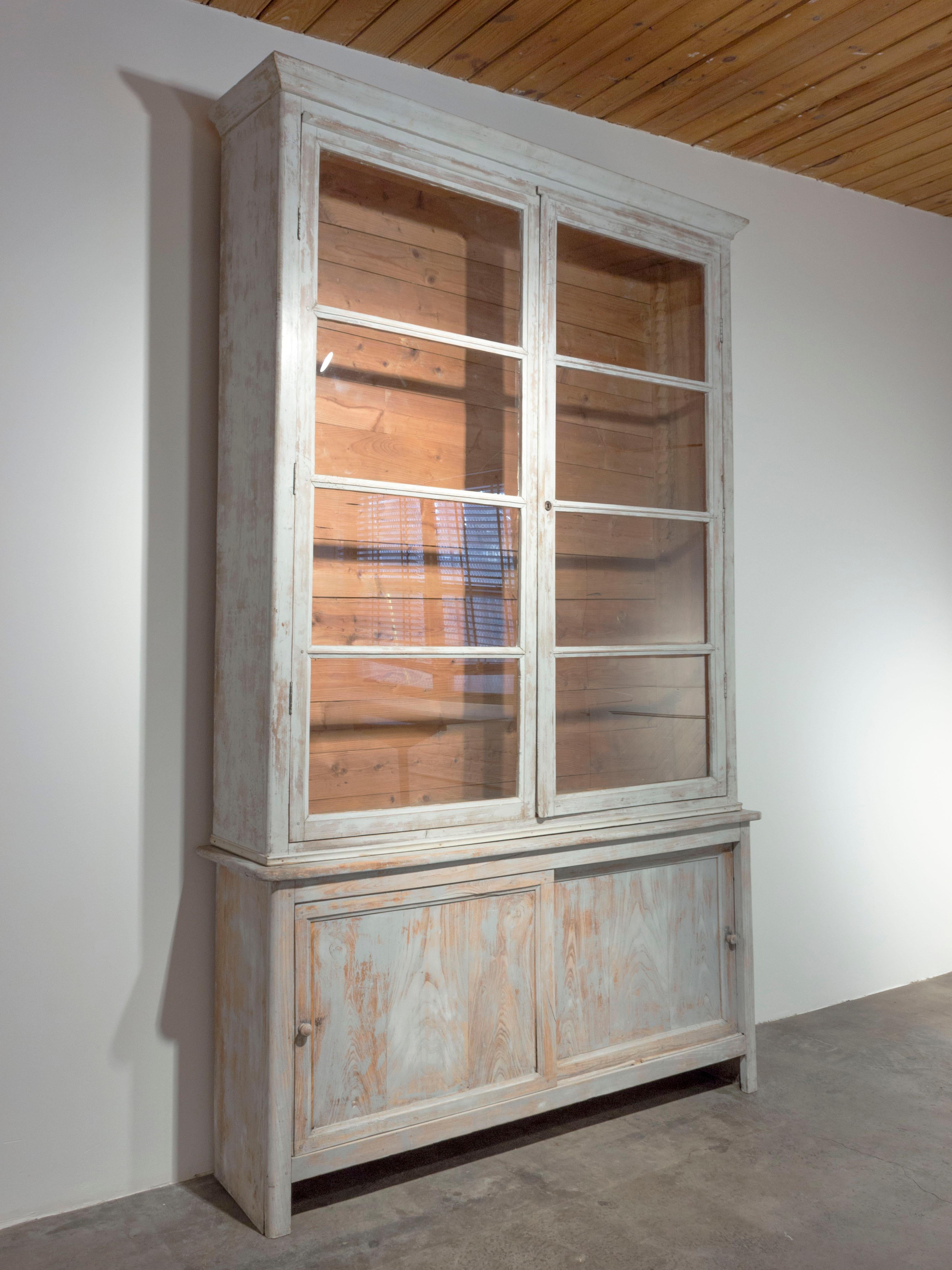 19th Century Swedish grey painted wood cabinet with glass front upper cabinet. Lower cabinet has sliding doors with wood knobs. 

Thin crack in one glass pane as shown. One shelf in lower cabinet, no upper shelves.