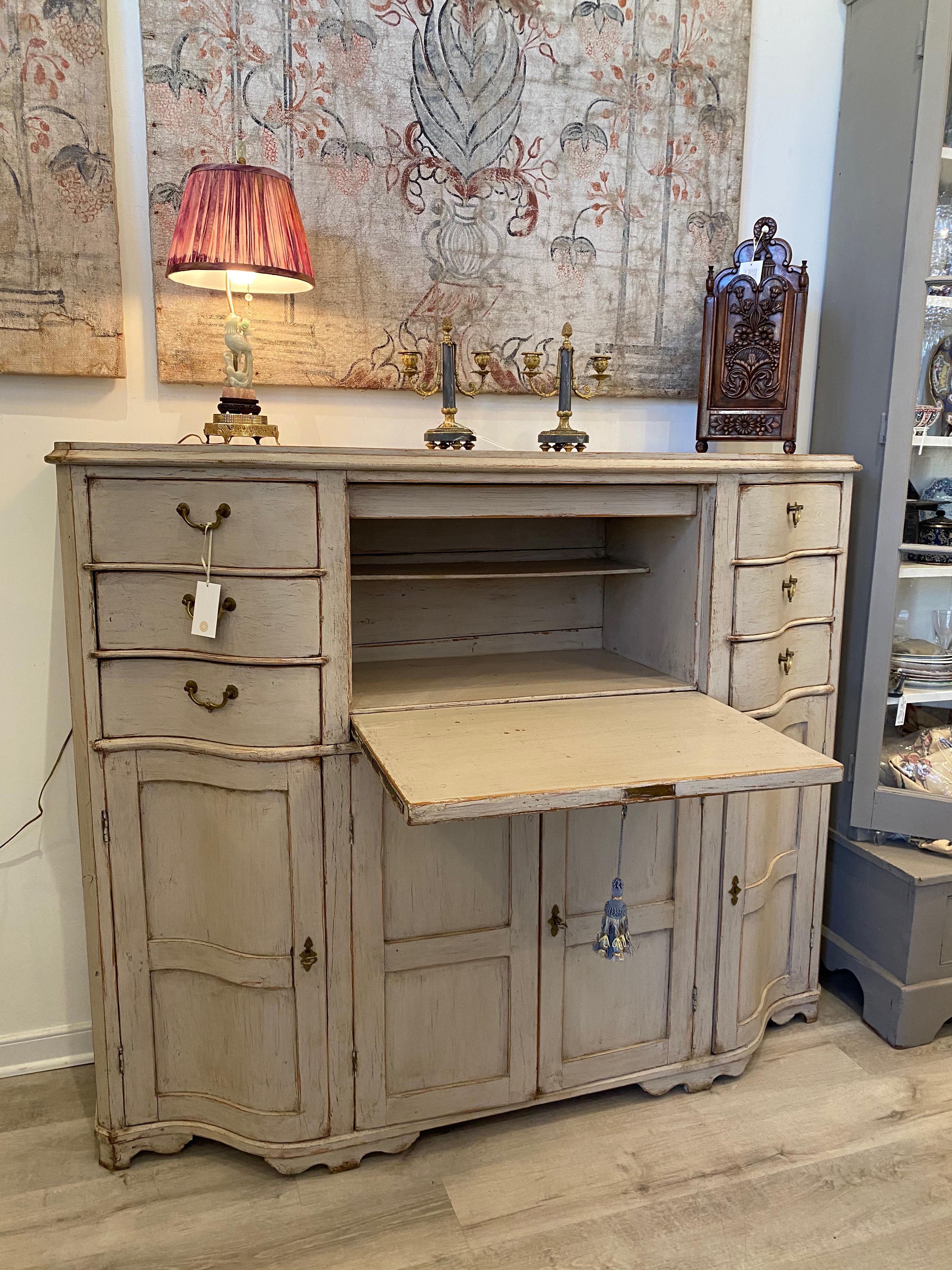 19th century Swedish painted desk/bureau. The serpentine top over a drop-down desk flanked by six drawers over a central cabinet having one shelf flanked by two cabinets having three shelves. Pine with a light grey polychrome.