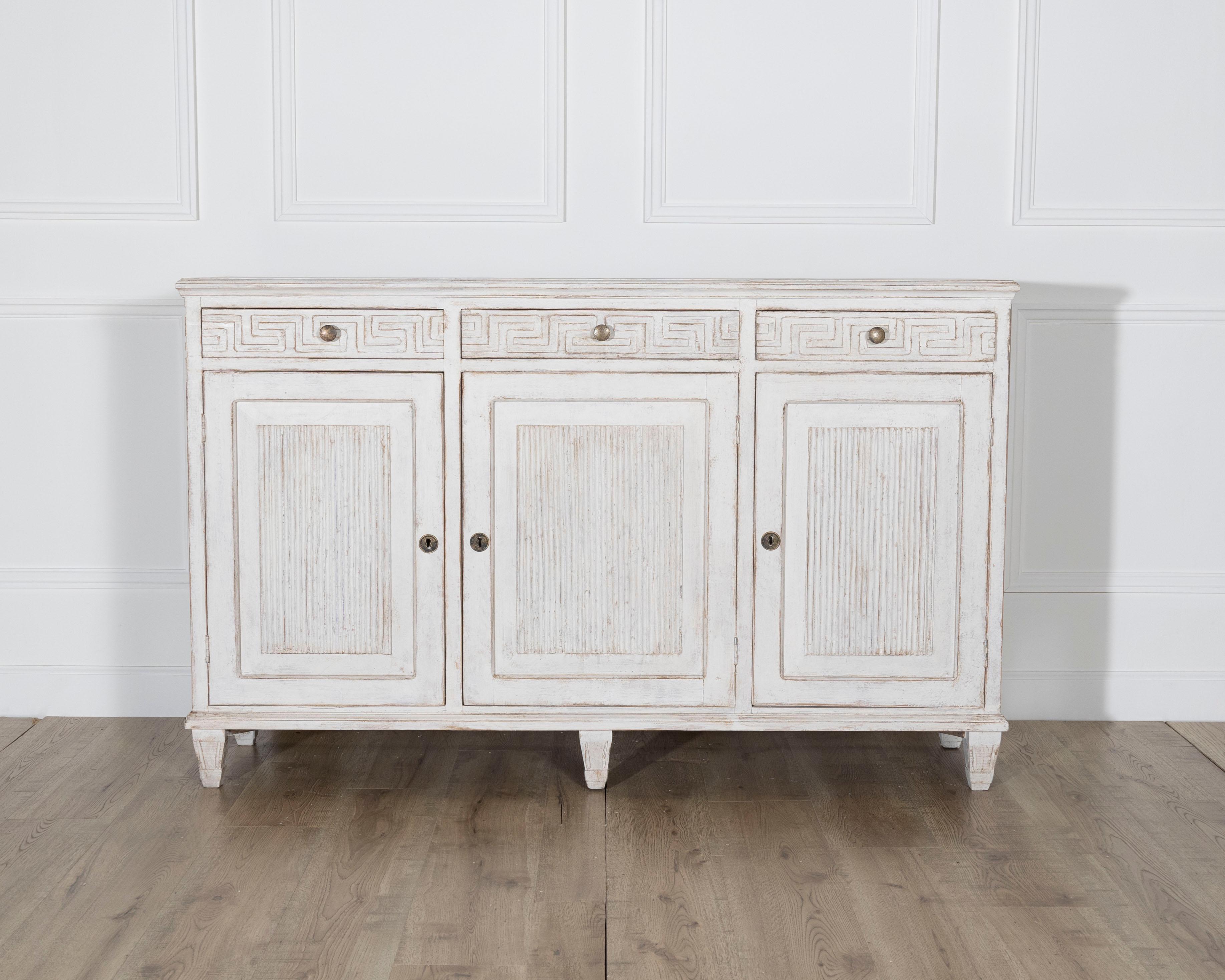 A striking 19th century Swedish sideboard in solid pine, showcasing a neoclassical sensibility and exceptional Scandinavian craftsmanship. The façade features three upper drawers, each adorned with a beautifully carved Greek key frieze, an iconic