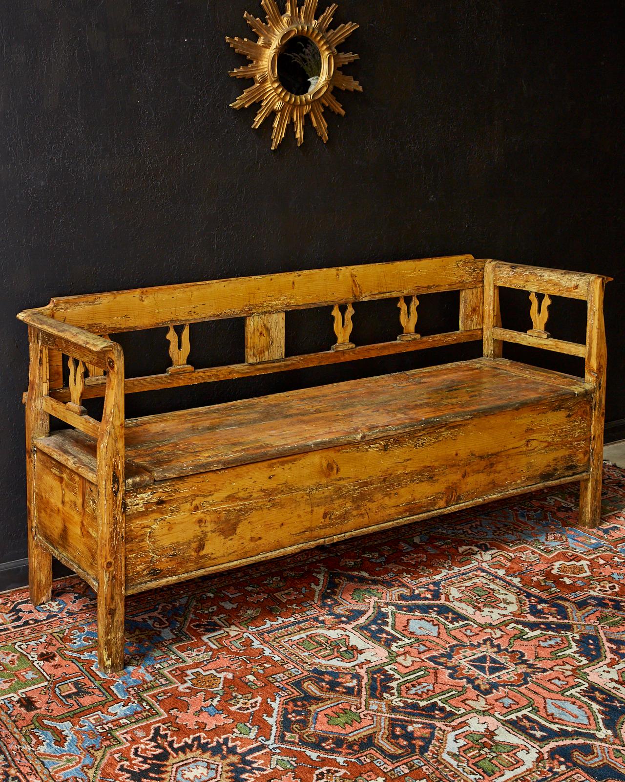 Rustic 19th century Swedish pine bench with a large storage drawer. Features a beautiful warm pine with a distressed, weathered, and worn finish. The back splat and sides are decorated with subtle rooster images. The storage box has original iron