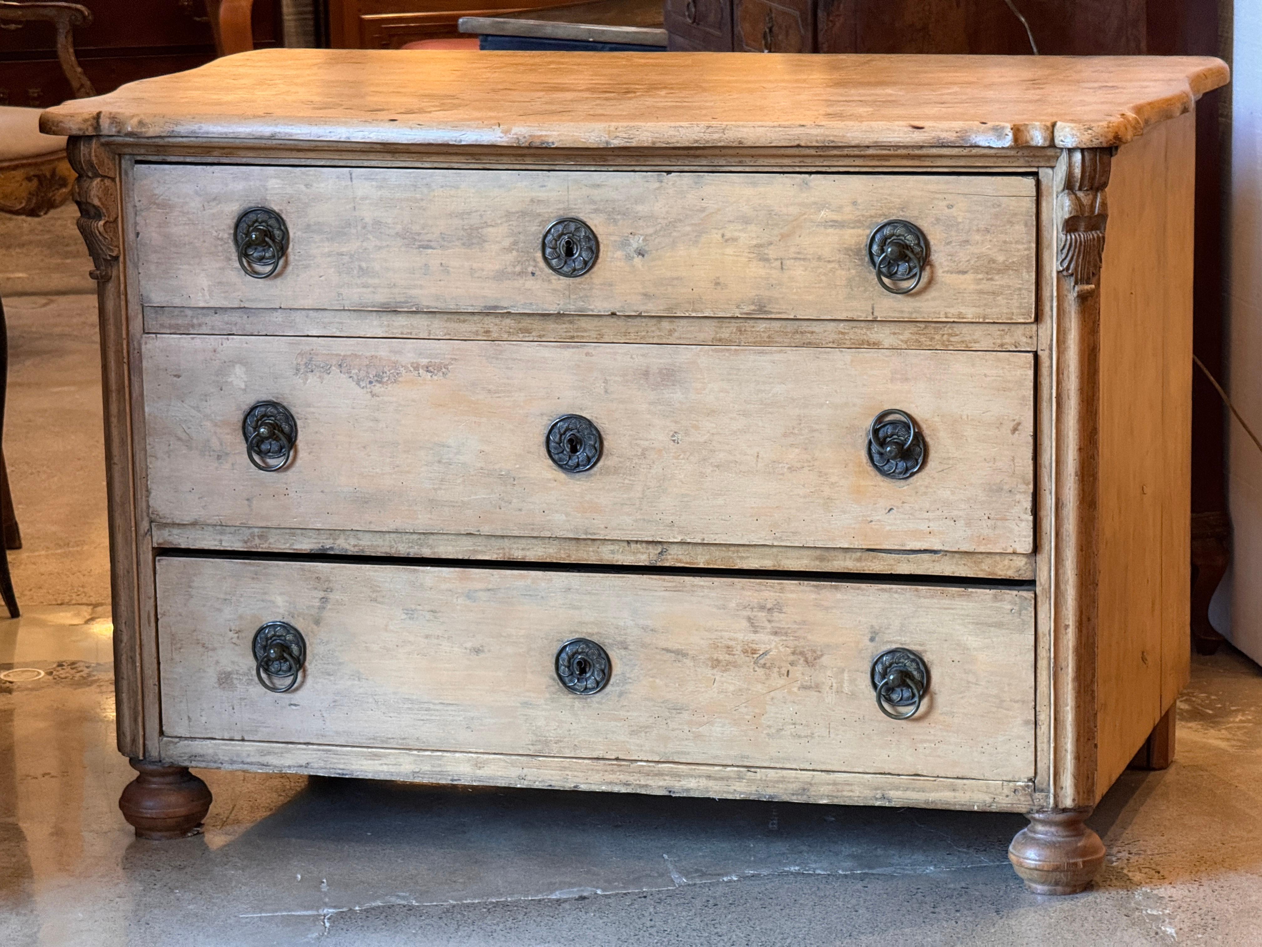 Commodo in pino svedese del XIX secolo con tre cassetti a tutta lunghezza e dettagli intagliati agli angoli. La finitura chiara e consumata e le linee pulite sono caratteristiche del gusto scandinavo, mentre i tiranti ad anello e gli intagli