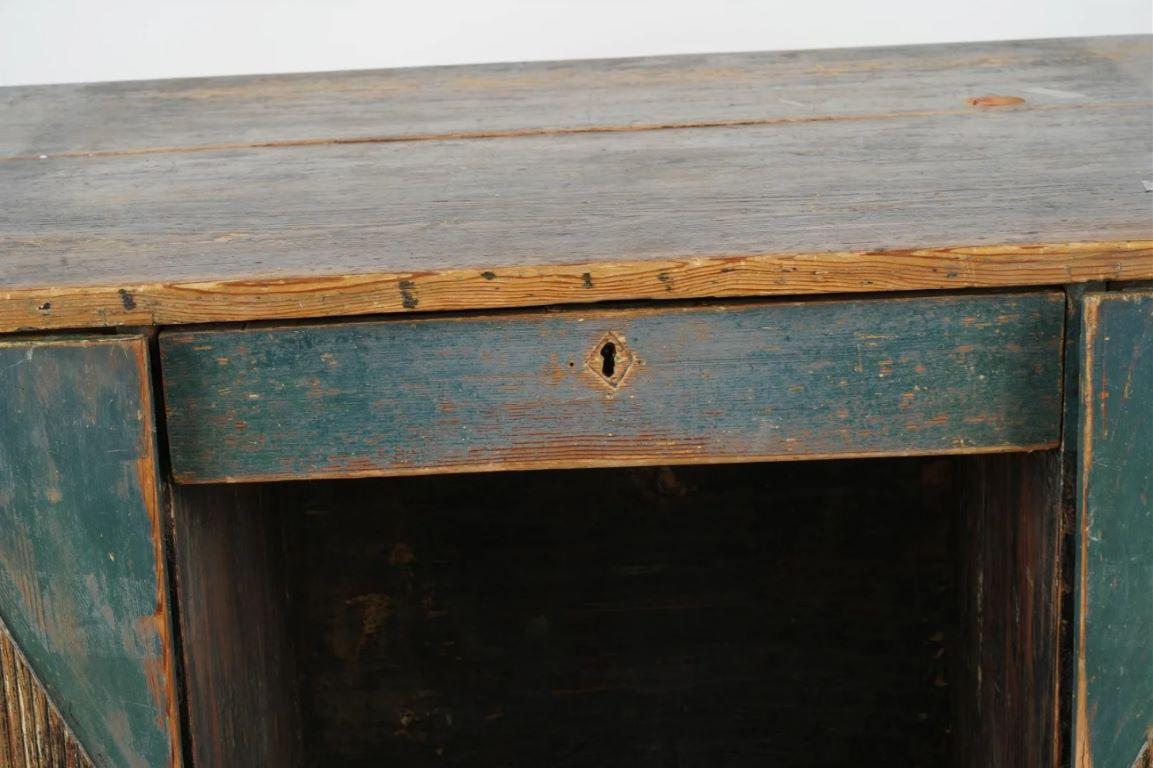 Bureau rustique suédois du début du XIXe siècle, peint en sarcelle, provenant de la collection personnelle de Dustin Hoffman. Deux portes latérales comportent des incrustations en bois sculpté en forme de diamant. 

Un côté équipé d'un tiroir