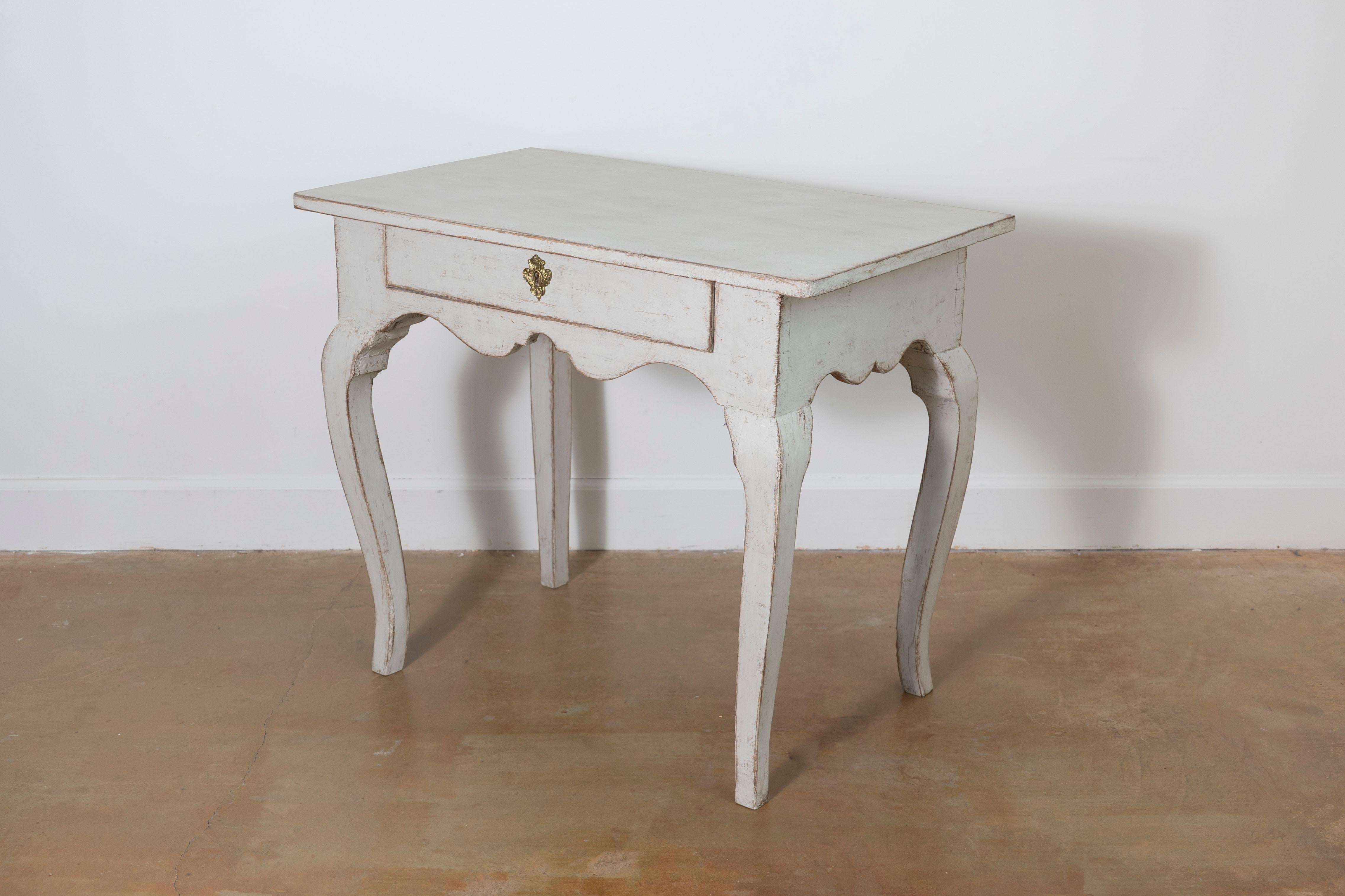 Dieser charmante schwedische Beistelltisch aus dem 19. Jahrhundert verkörpert die rustikale Eleganz des Gustavianischen Designs. Es ist aus Massivholz, wahrscheinlich Kiefer, gefertigt und mit einer gealterten Lackierung in einem weichen, gedämpften