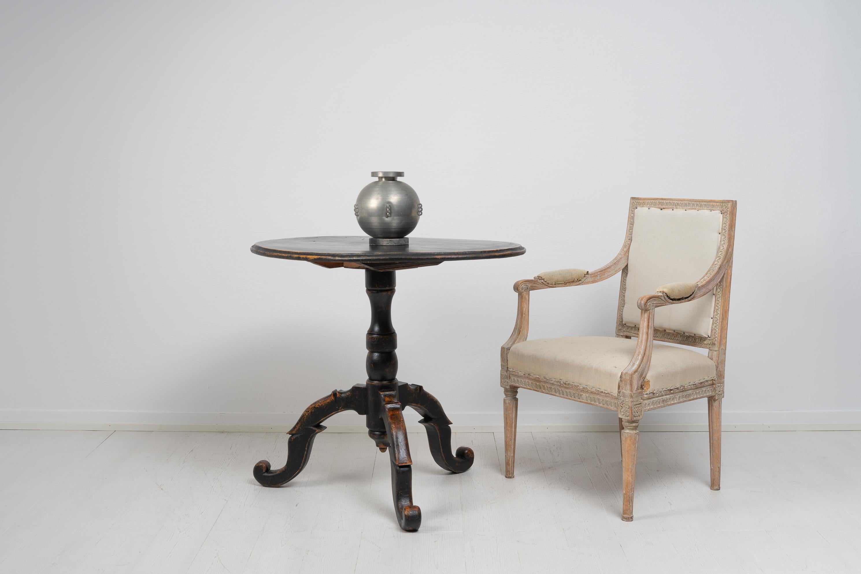 Schwedischer Tisch mit schwarzer Kippplatte aus der Mitte des 19. Jahrhunderts, um 1860. Der Tisch ist mit schwarzer Farbe gestrichen, die in Mitleidenschaft gezogen wurde, und das Holz darunter glänzt an einigen Stellen durch. Die Notlage verleiht