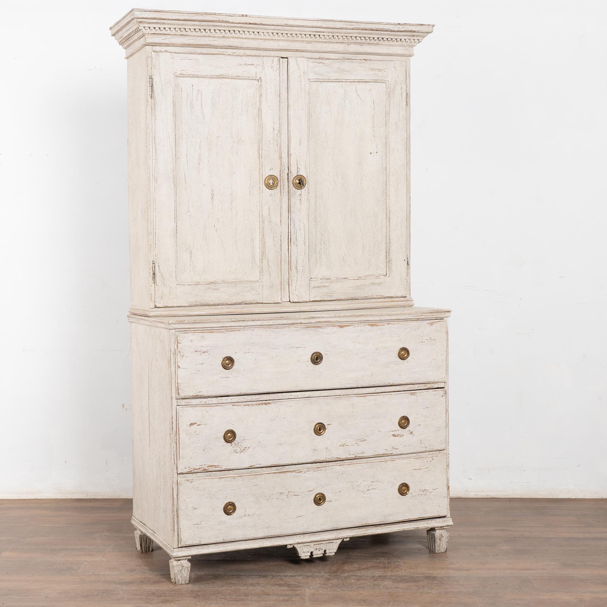 Beautifully crafted Swedish Oak Cabinet with dentil molding along the crown, standing 7' tall.
Newer custom professionally painted finish in layered shades of antique white and lightly distressed to fit the age and grace of this lovely cabinet.