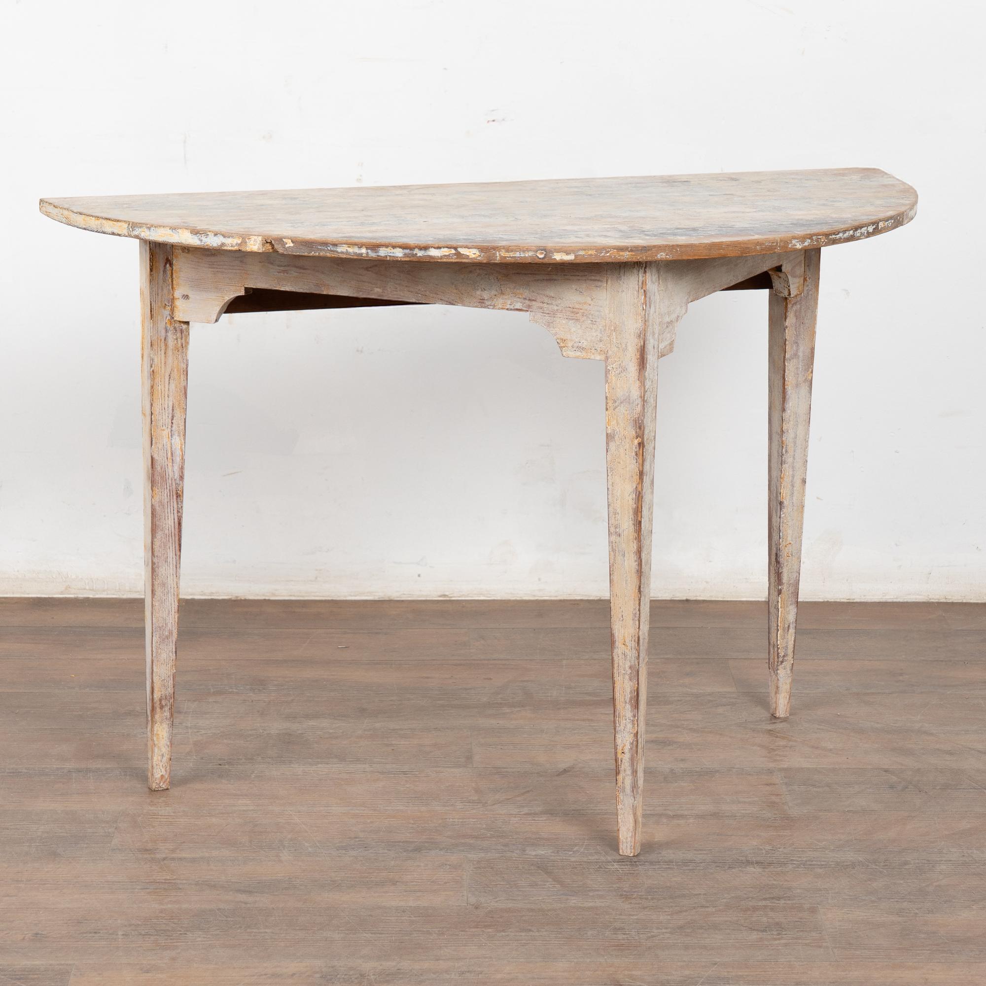 Single demi-lune side table with simple Swedish design and gently tapered legs.
Original white and cream paint scraped and distressed down to the natural pine, fitting the age and rustic country look of this console.
Restored, strong and stable,