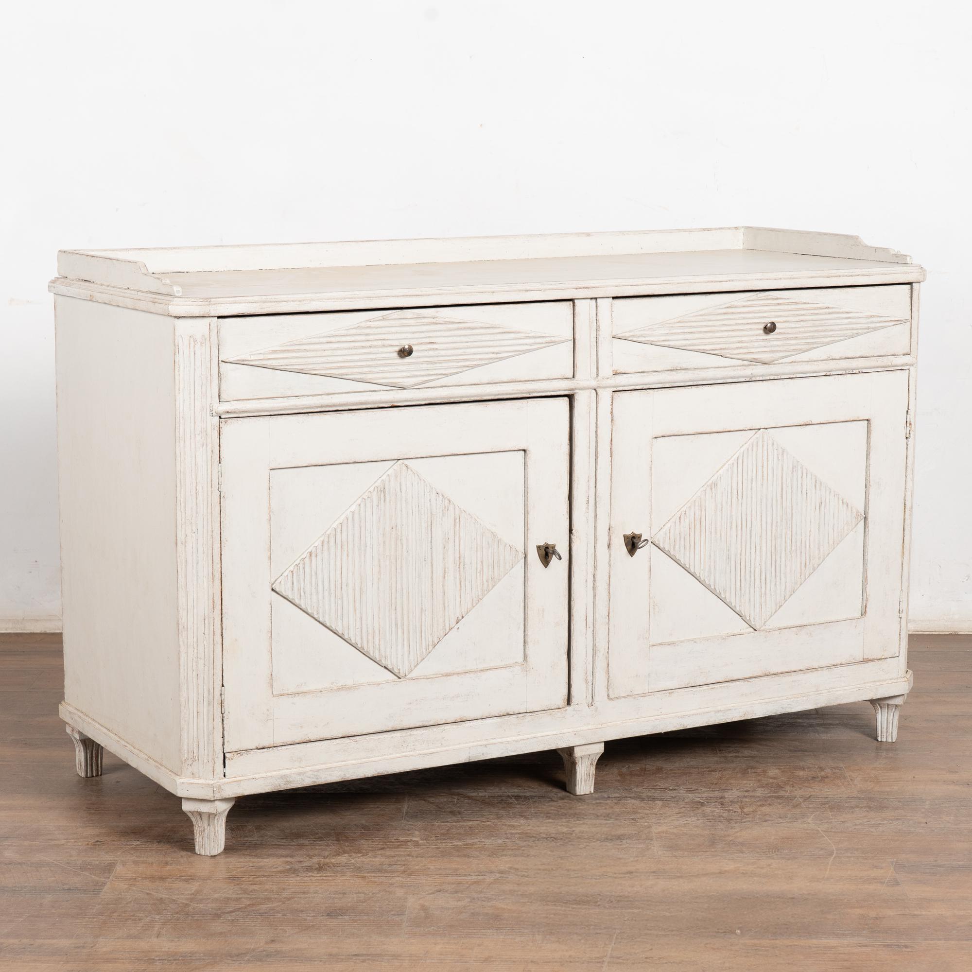 Gustavian pine sideboard or serving buffet with traditional decorative fluted diamond panels on cabinet doors and drawers.
The newer, professionally applied antique white painted finish with gray undertone is slightly distressed, fitting the age and