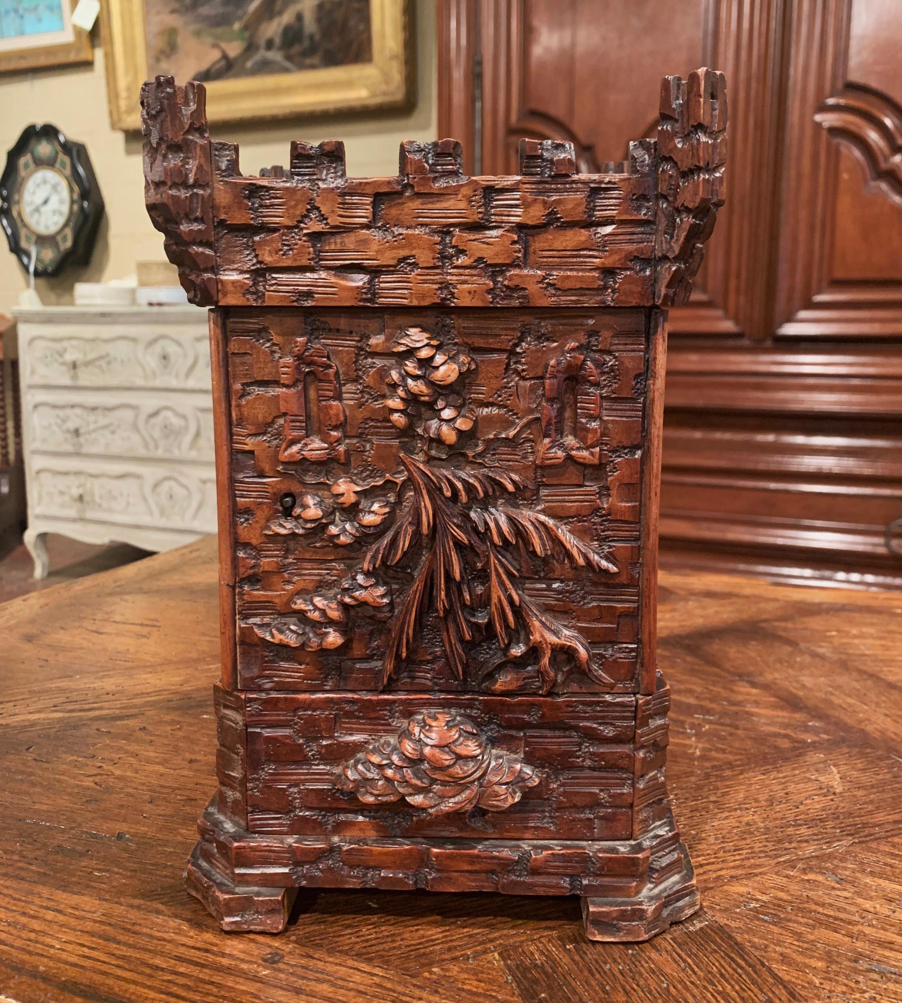 Crafted in Switzerland circa 1880, the carved cigar box is shaped as a castle tower. The box is decorated with carved foliage motifs and features a center door with two inside adjustable cigar shelves, and a bottom drawer for matches and cutter. The