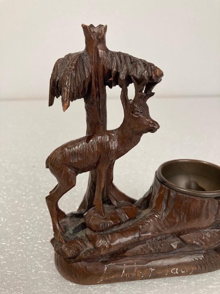 Sweet little Black Forest carving of a stag standing near a pine tree next to a brass lined nut or candy dish. Some writing bottom front in white is too worn for me to make out, probably the town where the carving was done. 
Measures: 5.5 inches