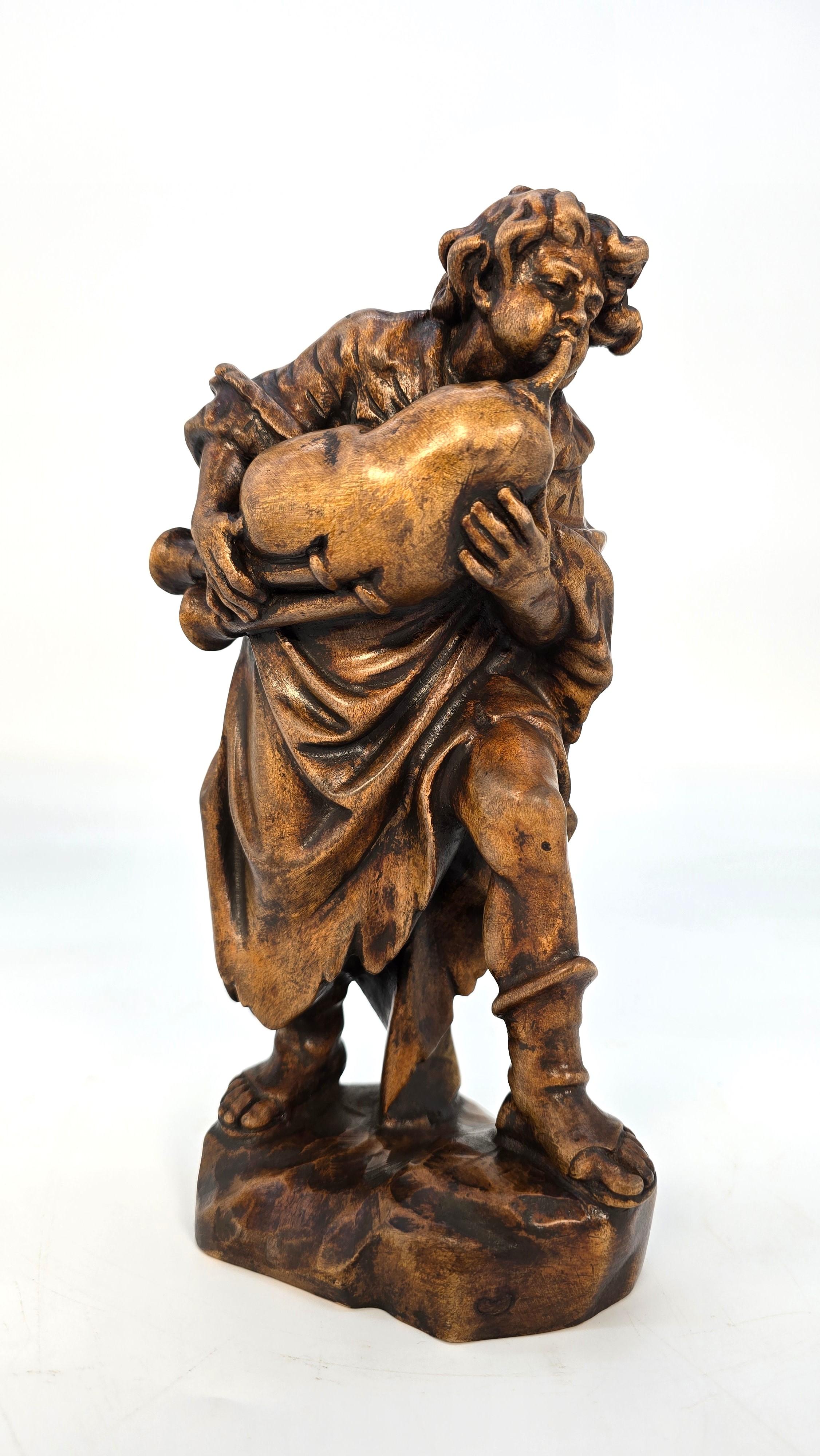 A Black Forest hand-carved limewood figure portrays a young man from the medieval period dressed in a cloaked tunic and open-toed boots playing a set of traditional Swiss bagpipes called Schweizer Sackpfeife. This handmade wind instrument, similar