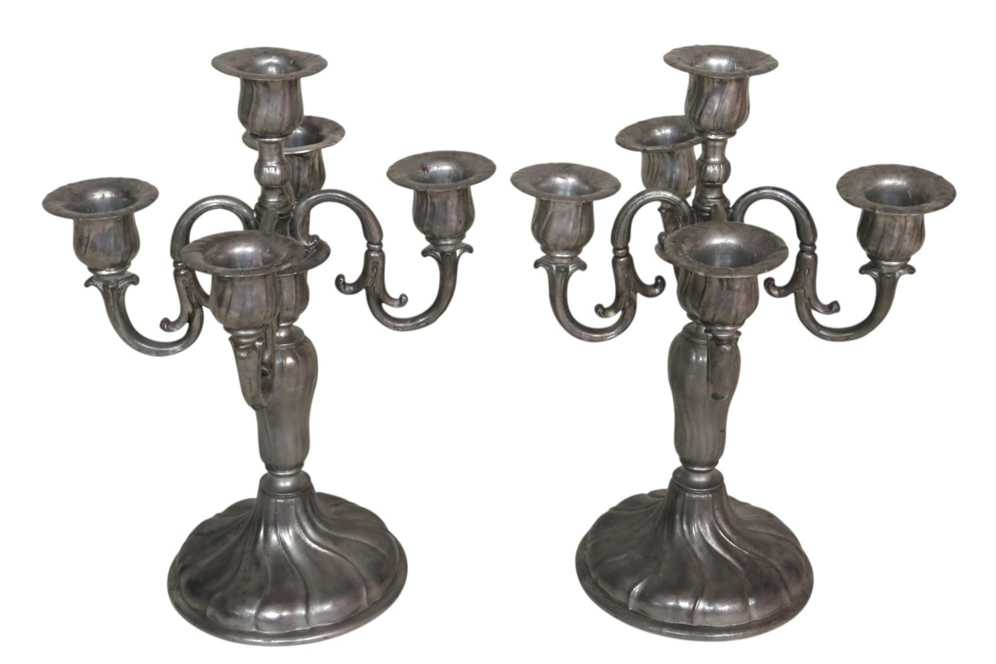 Paire de candélabres suisses en étain de la fin des années 1800. Elle contient cinq bougies, avec une colonne centrale tournée qui supporte quatre bras courbés. Chacun d'eux est surmonté d'un chapiteau épuré, pressé avec des lignes ondulées qui