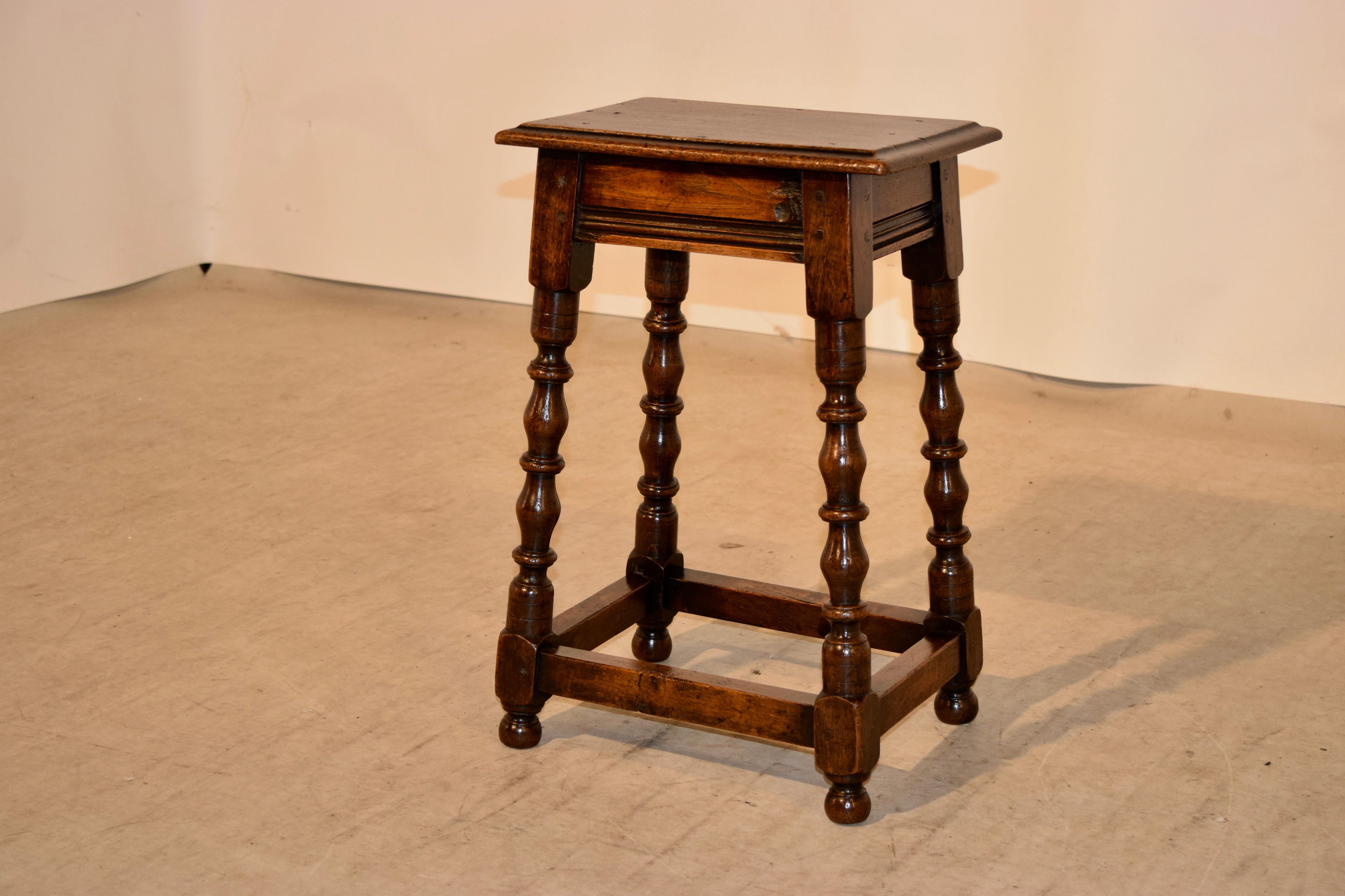19th century English oak tall joint stool with a beveled edge around the top following down to a routed decorated apron and supported on hand turned and splayed legs joined by simple stretchers and raised on hand turned feet. Pegged construction.