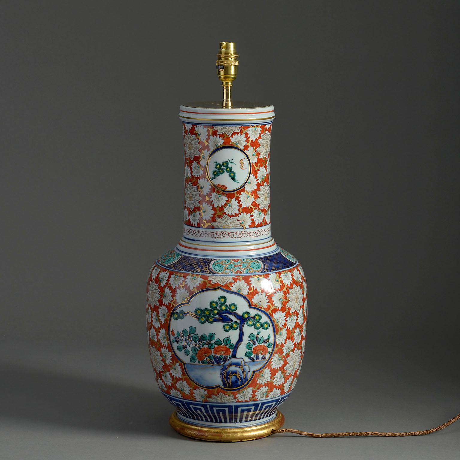 A tall late nineteenth century Imari porcelain vase of gourd form, decorated in the traditional manner with glowers and foliage on a red ground, with cartouches throughout depicting spring blossoms. Mounted as a table lamp on a hand turned giltwood