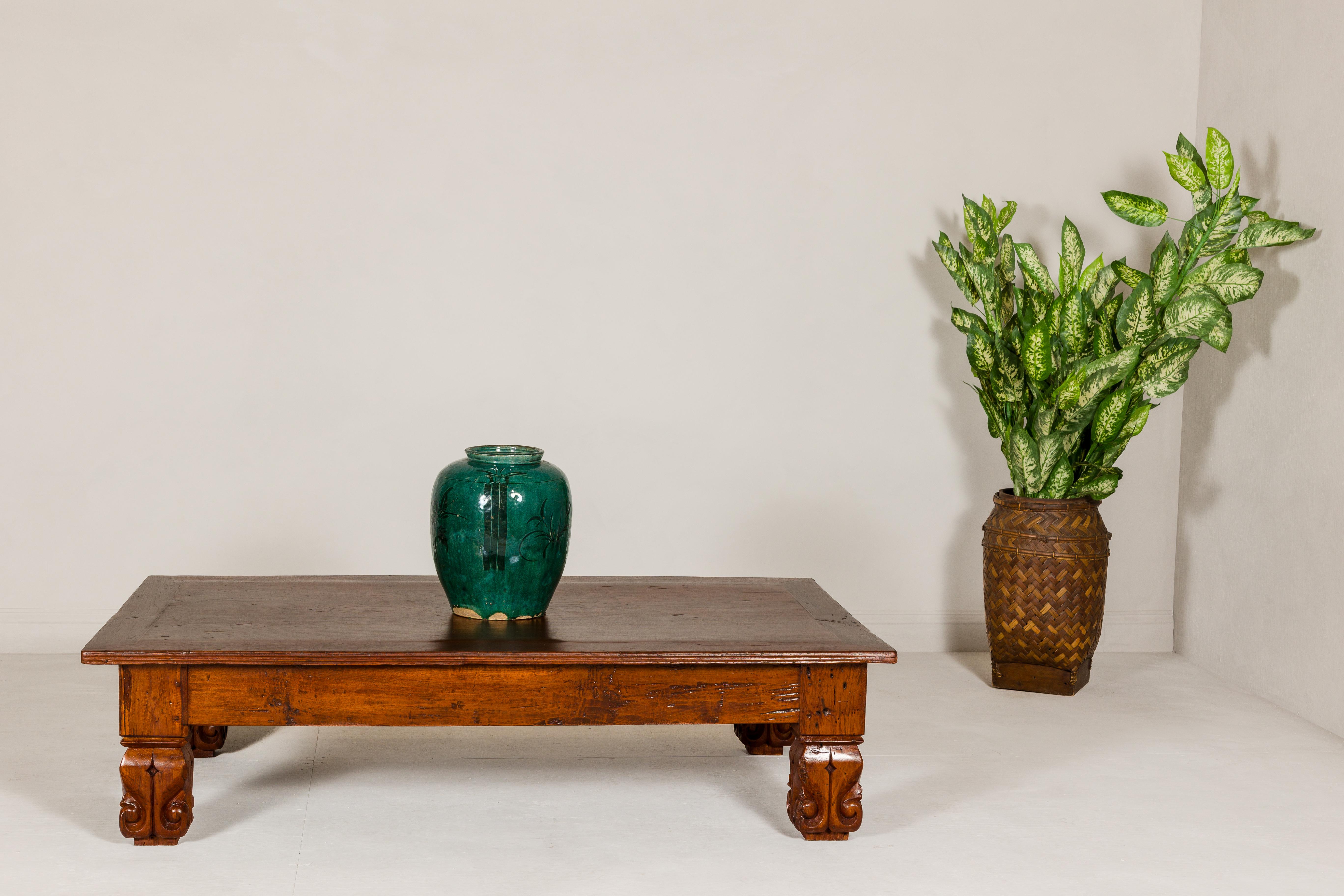 A teak wood low coffee table from the 19th century with carved legs and brown patina. This 19th-century teak wood coffee table is a true testament to the enduring beauty of antique craftsmanship. Its simple yet sturdy design, combined with a rich